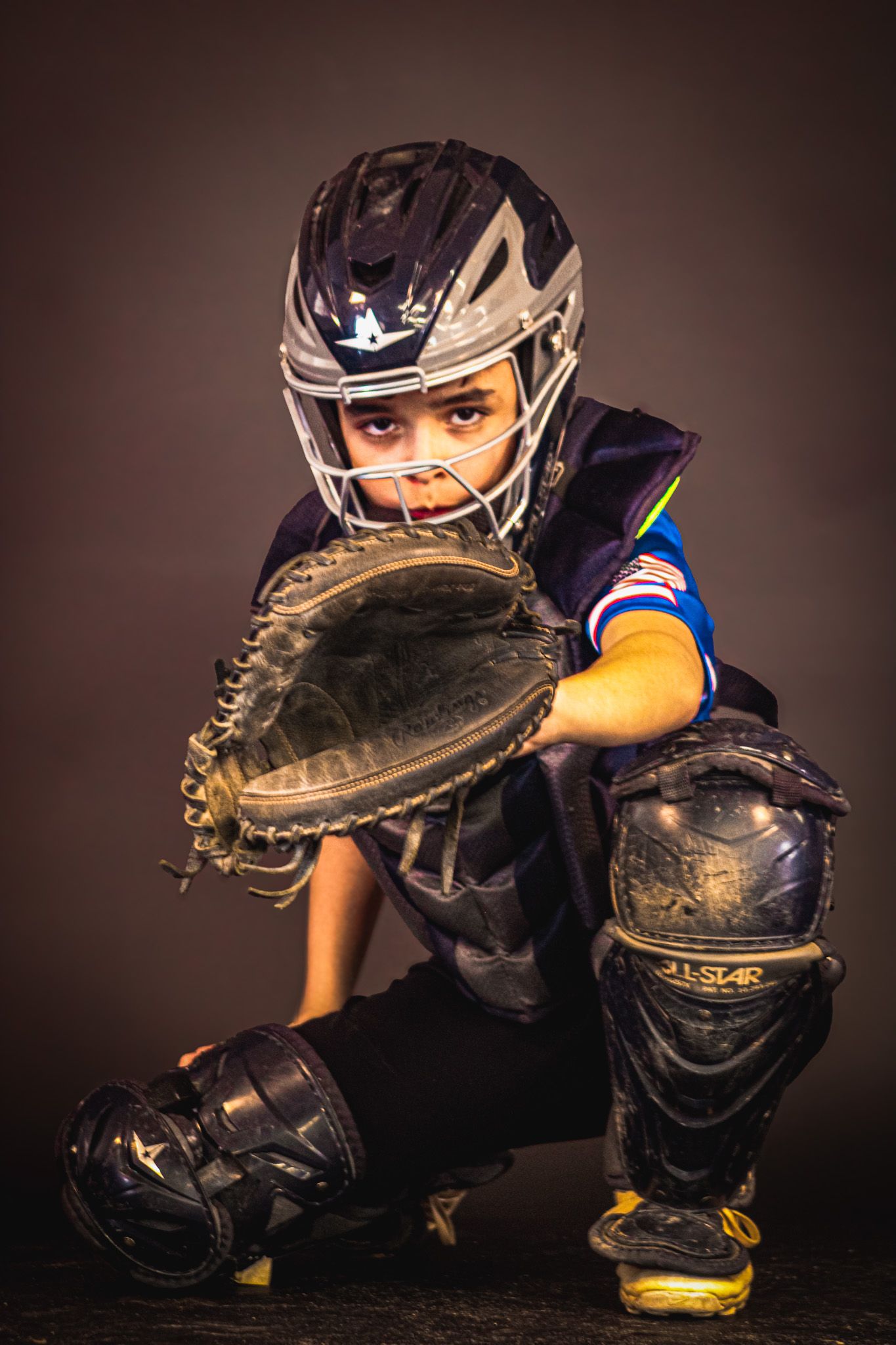 Young baseball catcher in full gear, crouching in ready position with mitt extended, wearing helmet and chest protector. sports
