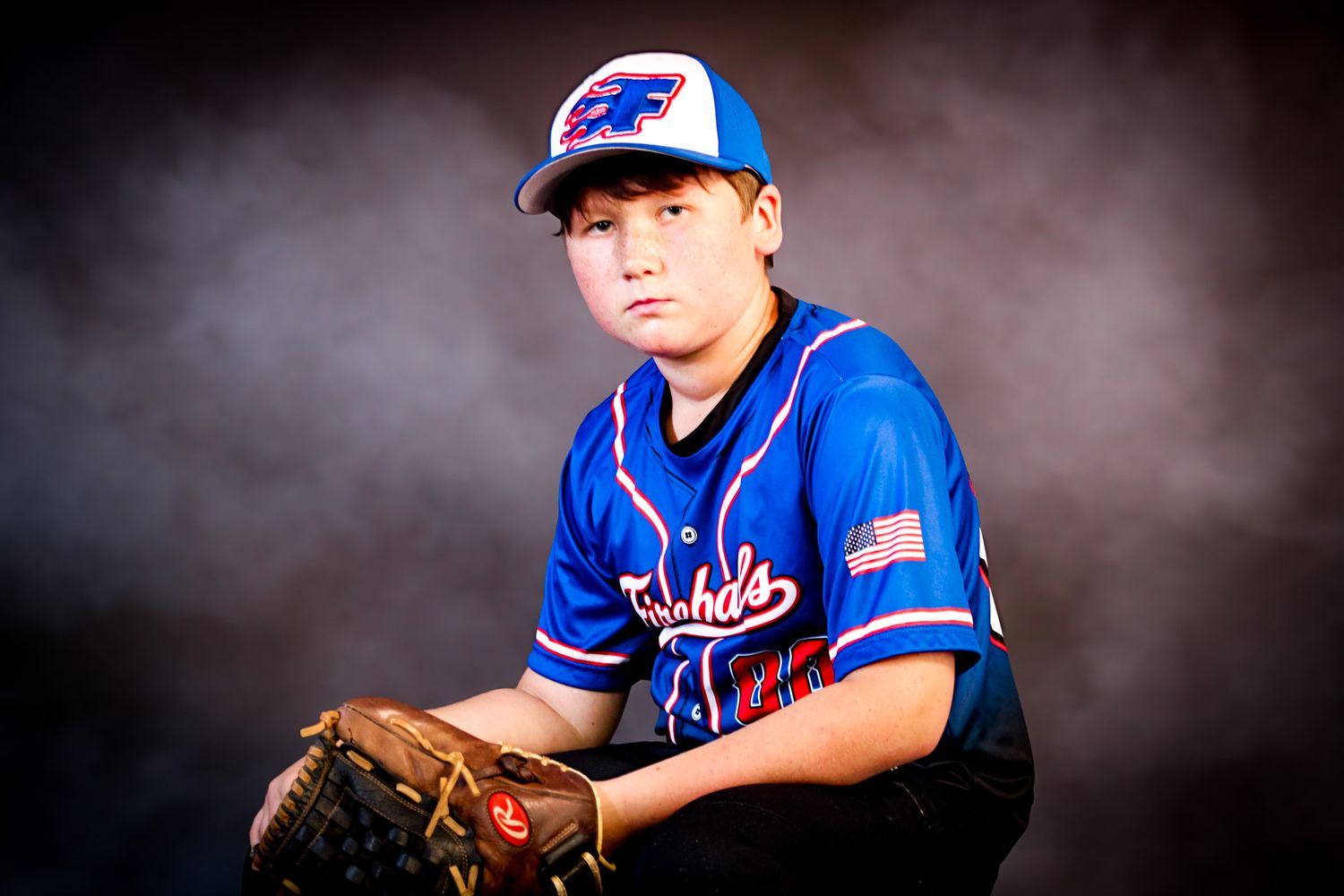 Young baseball player in Fireballs uniform posing with glove in dramatic studio lighting. sports