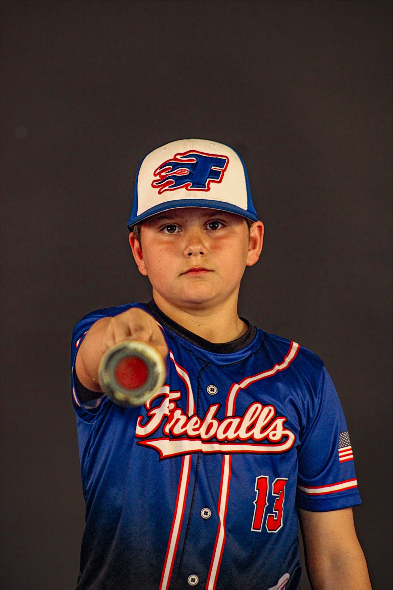 Young baseball player in Fireballs jersey number 13 pointing bat toward camera in studio portrait. sports