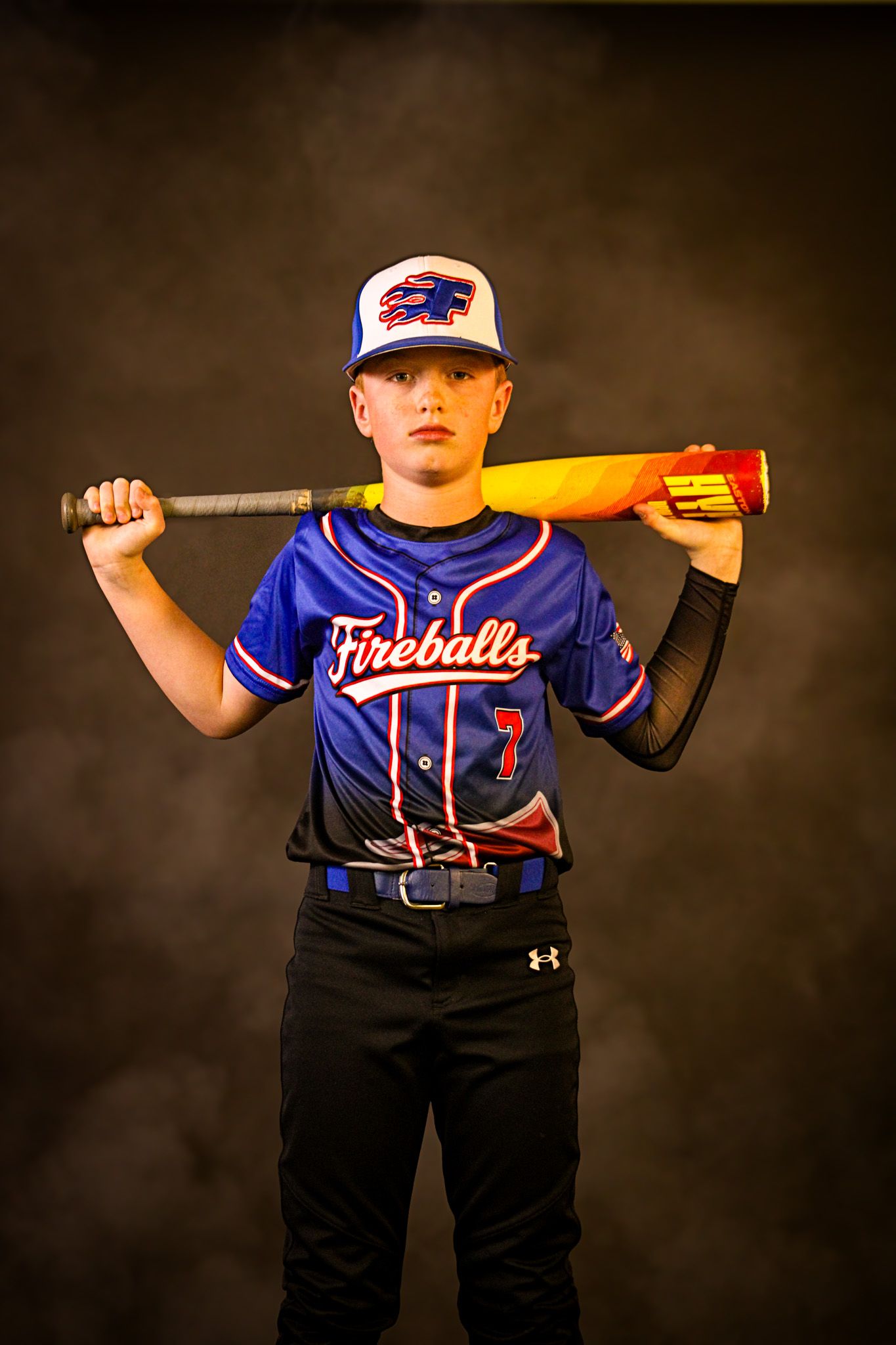 Youth baseball player in Fireballs jersey number 7 holding bat behind shoulders in studio. sports
