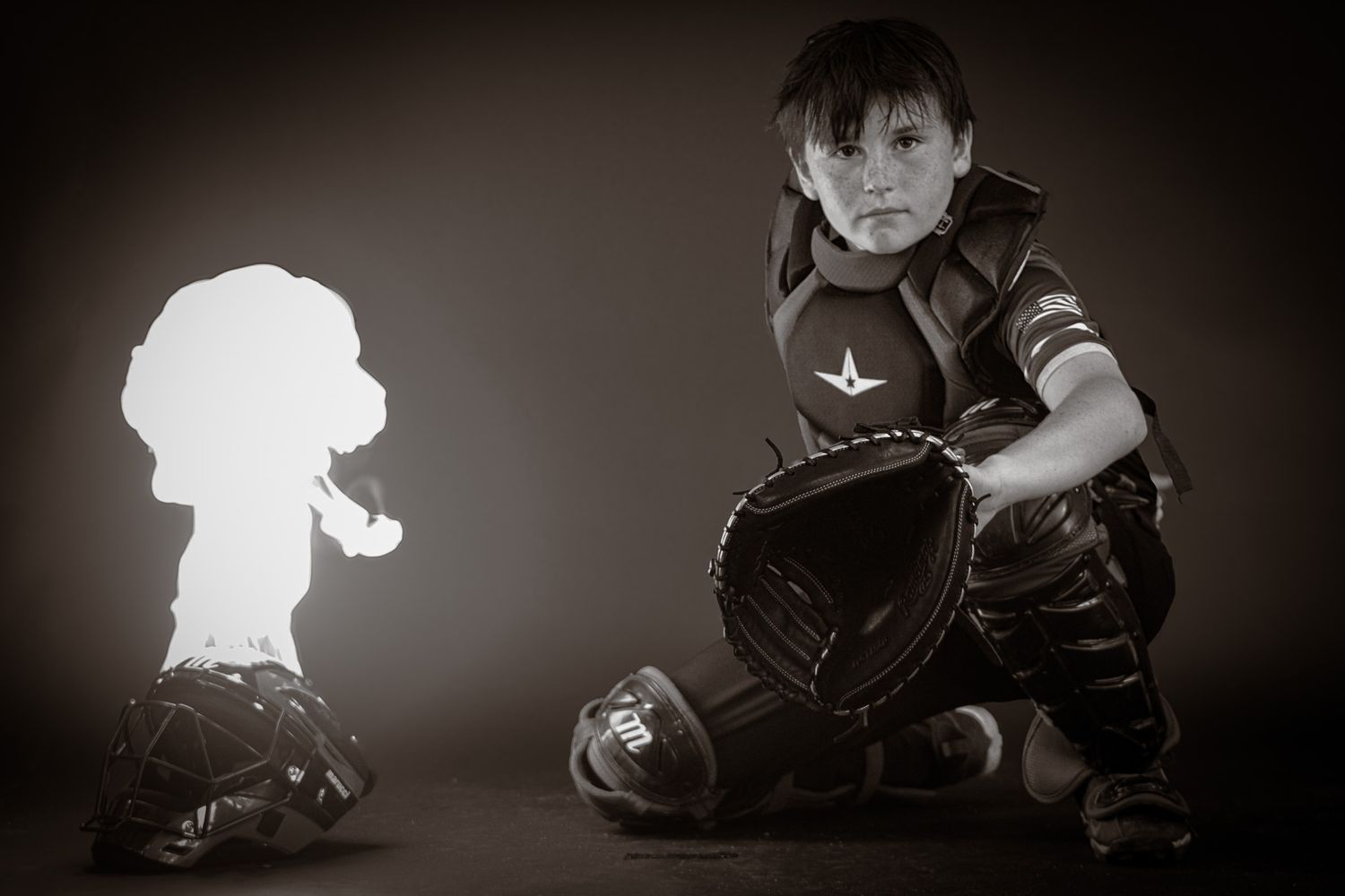 Young boy in full baseball catcher gear posing dramatically in black and white studio photo. sports