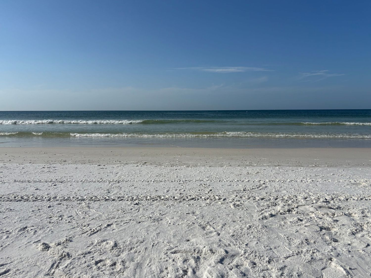 White sandy beach with turquoise ocean waves under a clear blue sky on a sunny day.