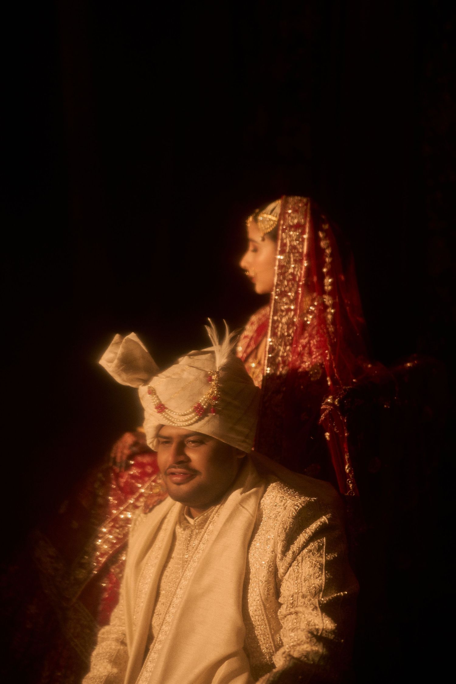 Indian bride and groom in traditional wedding attire, groom in white sherwani and turban, bride in red dupatta.