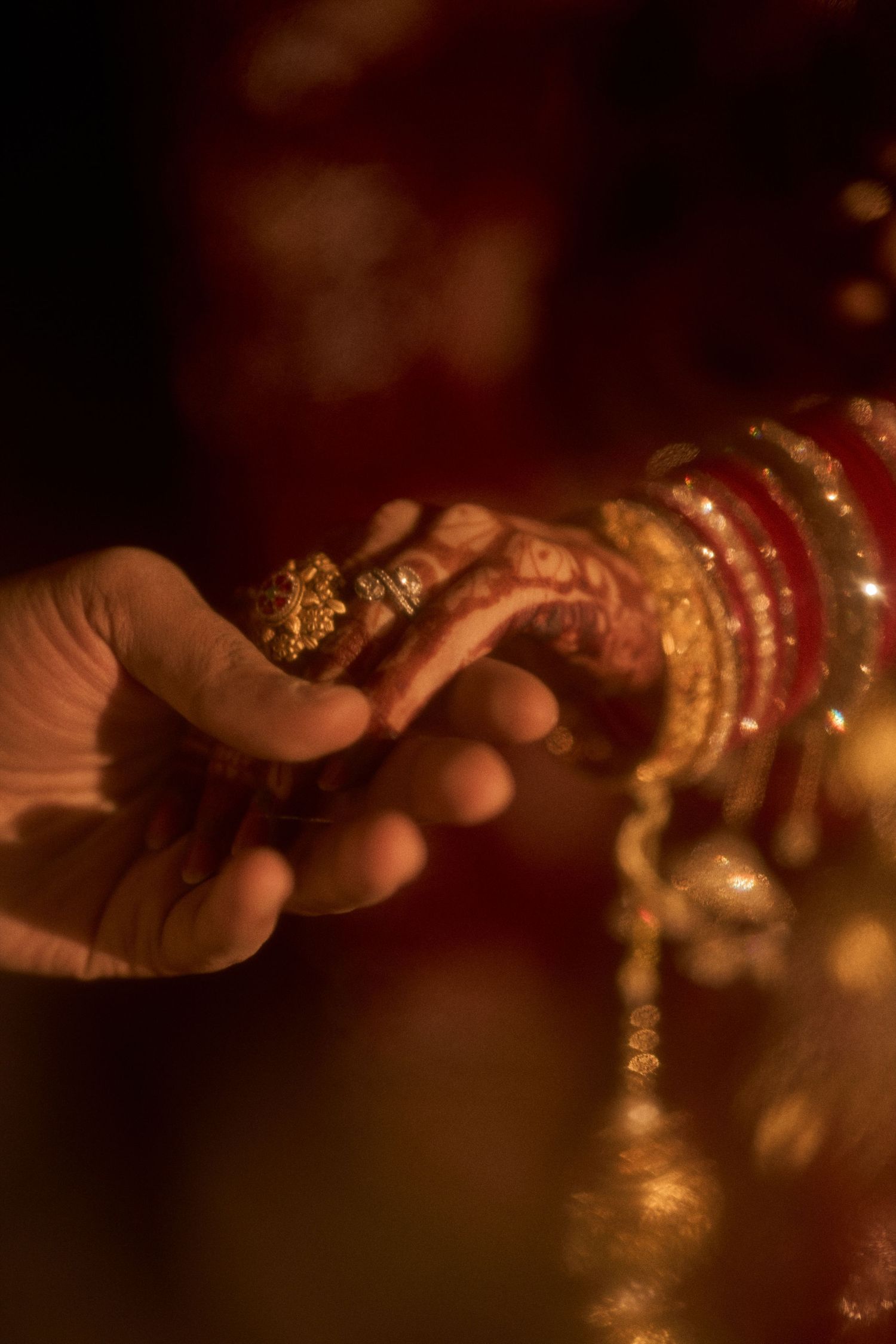 A bride adorned with gold bangles and mehndi receives a gold ring from a groom during an Indian wedding ceremony.