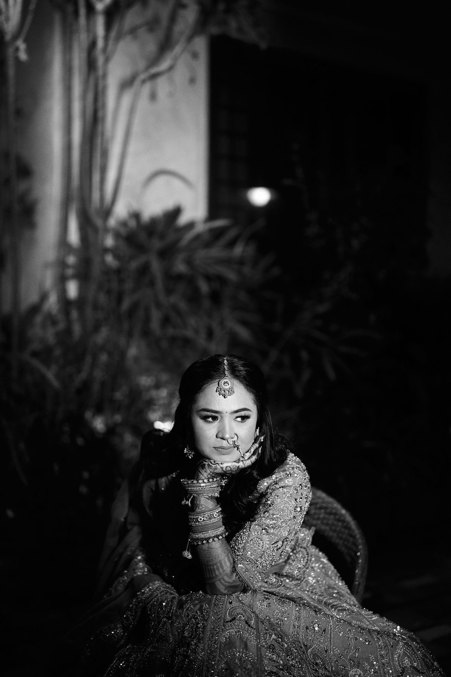 Elegant Indian bride in embroidered lehenga poses thoughtfully in a moody black and white portrait.