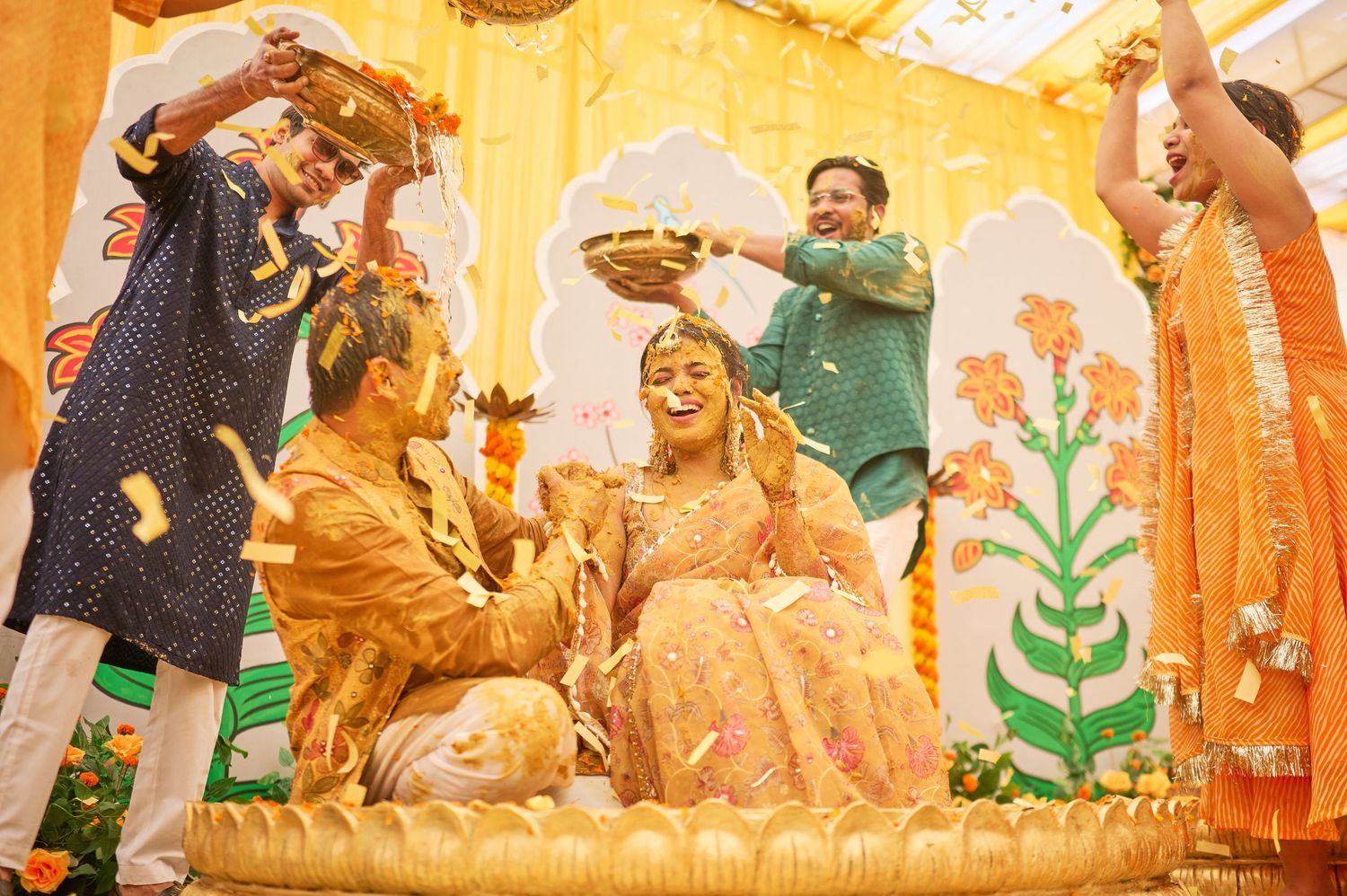 Joyful Indian Haldi ceremony with couple covered in turmeric paste, surrounded by family celebrating.