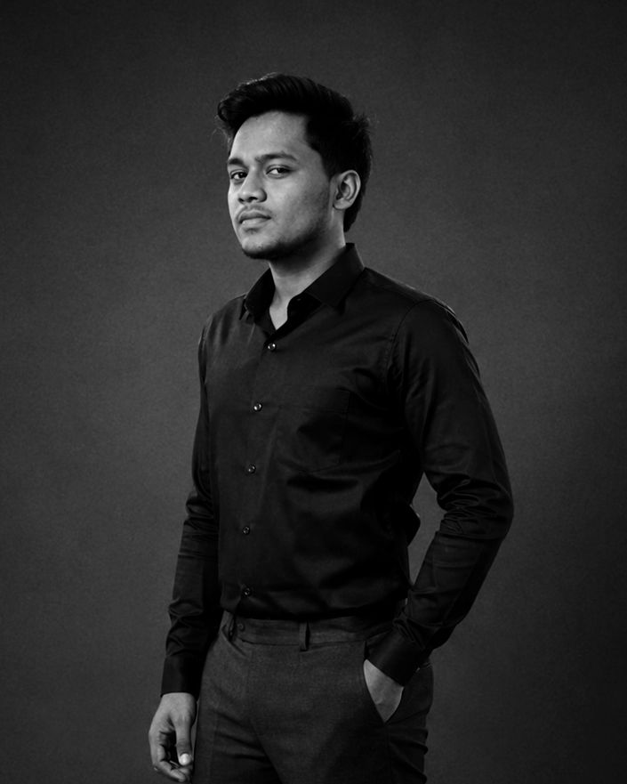 Black and white portrait of a young man in a black dress shirt, posing confidently against a dark studio background.
