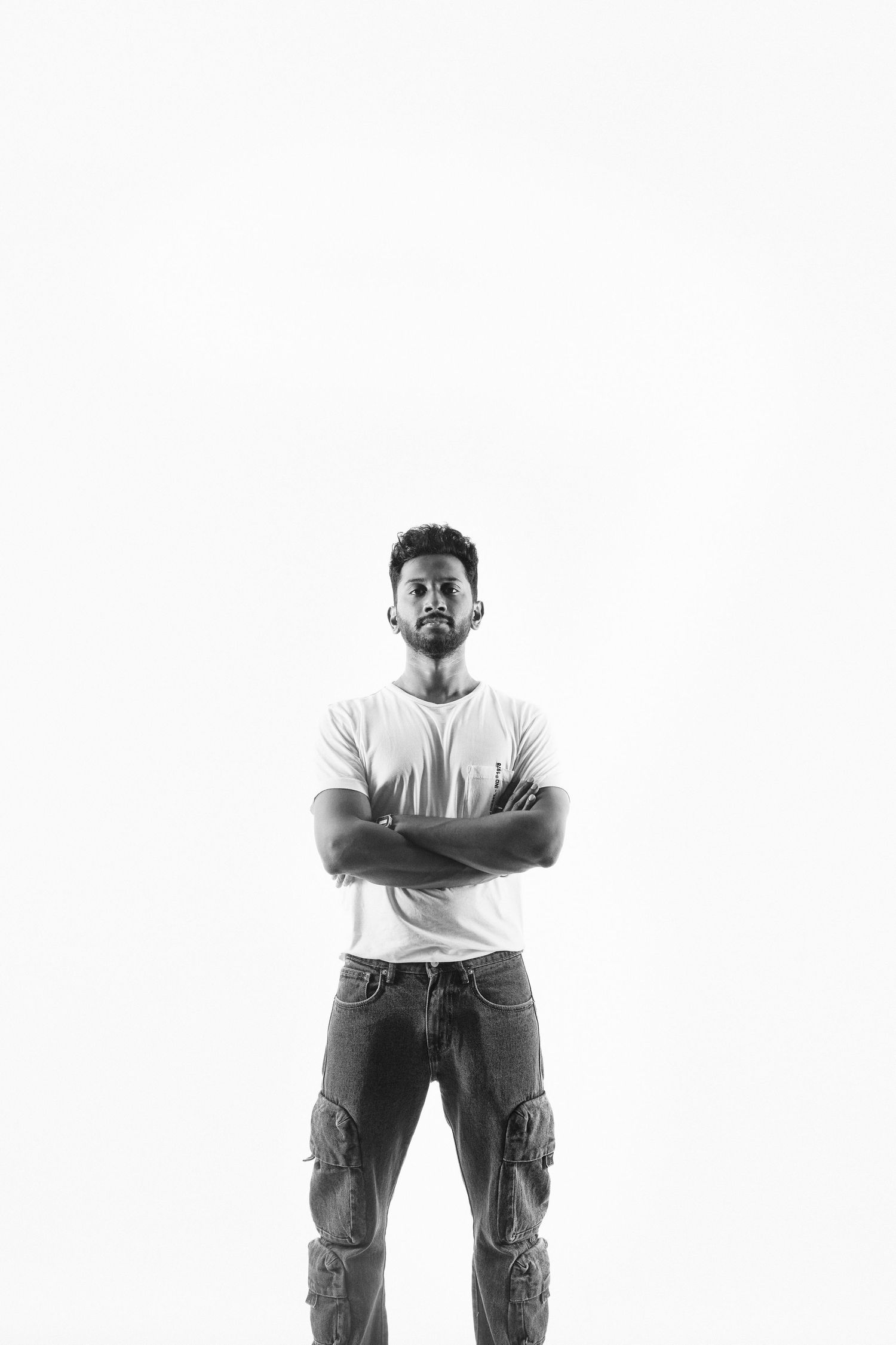 Confident young man with crossed arms in white t-shirt poses in black and white studio photo.