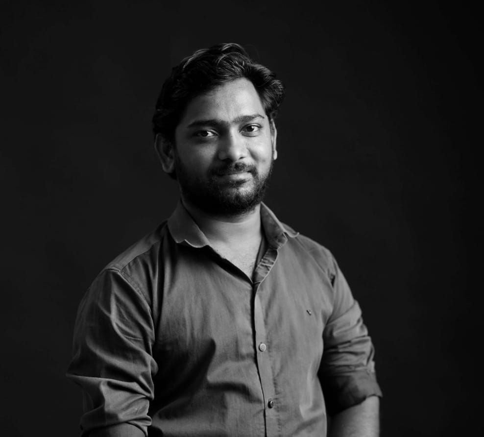 Black and white portrait of a young bearded man in a button-up shirt against a dark background.