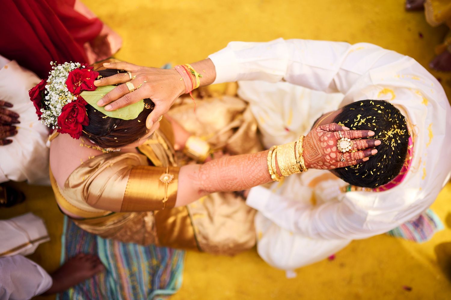 Close-up of Indian wedding ceremony hands with henna, gold bangles, and flower garlands exchanging ritual offerings.