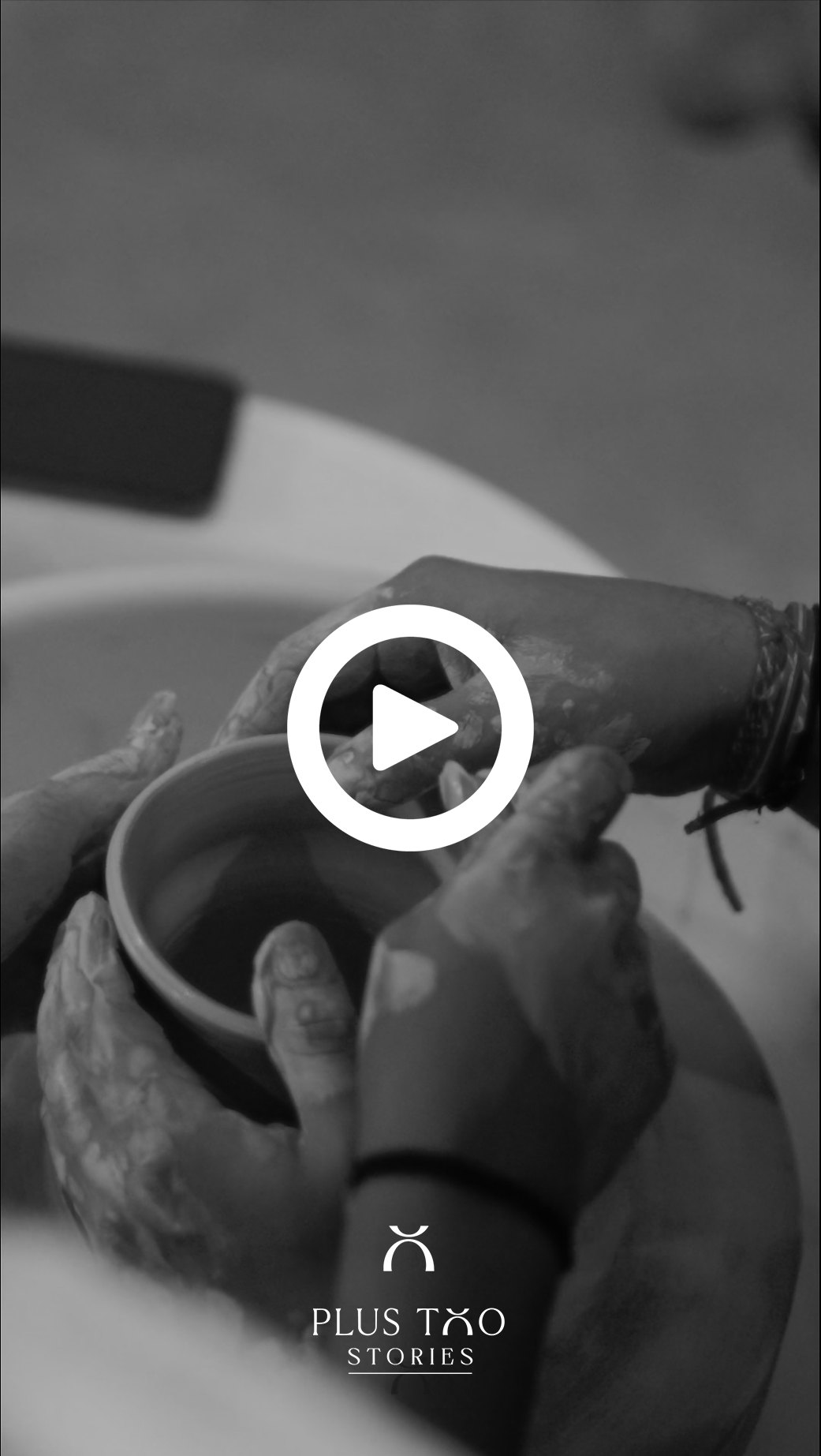 Black and white video thumbnail of hands shaping clay on a pottery wheel, with Plus Two Stories branding.