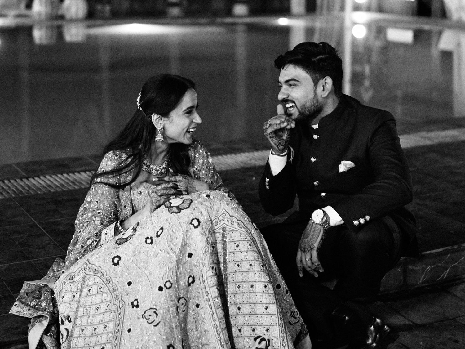 Couple in traditional Indian wedding attire sharing a joyful moment, black and white photography.