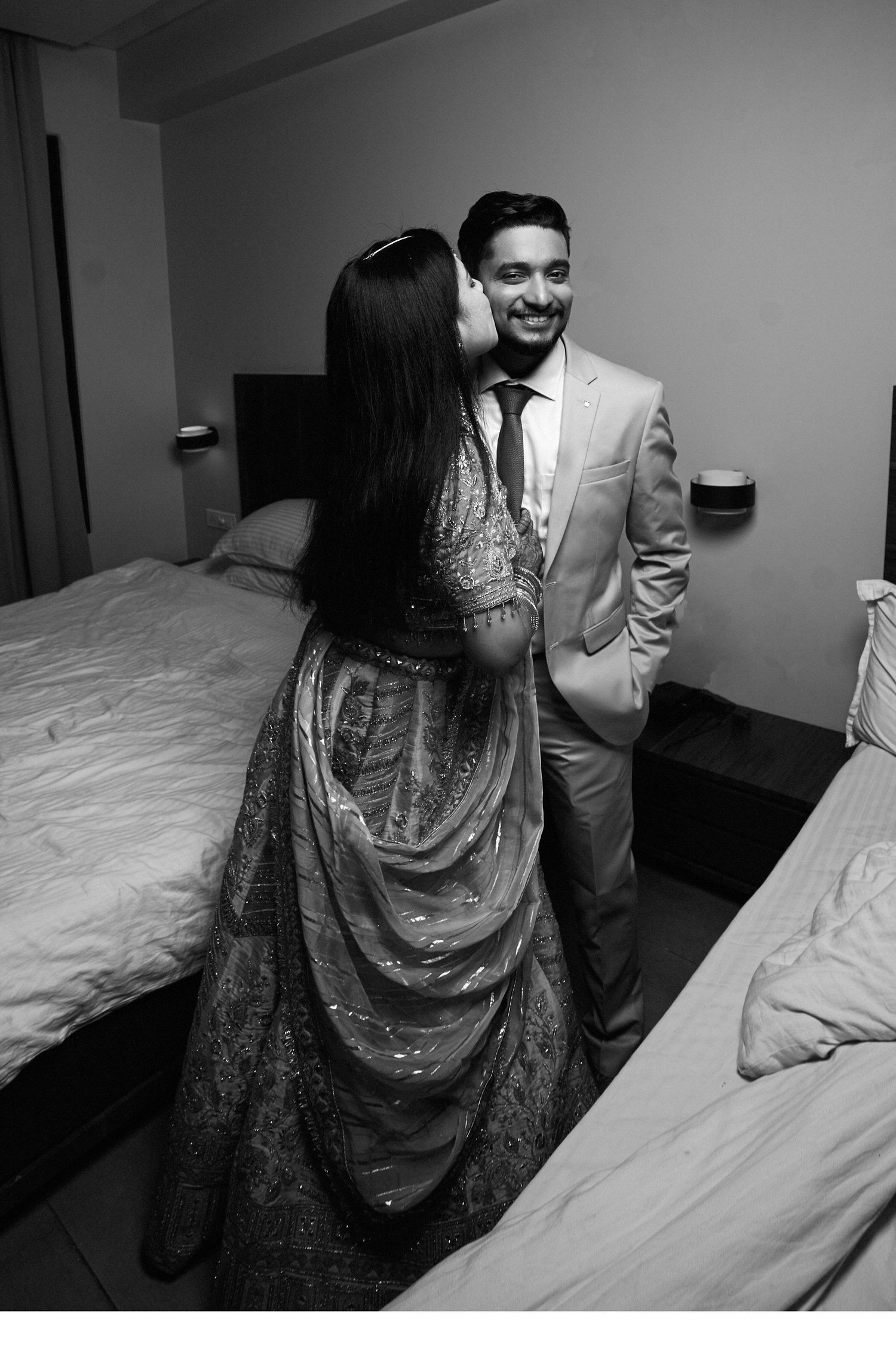 Black and white photo of a couple in formal attire sharing a romantic moment in a hotel room.