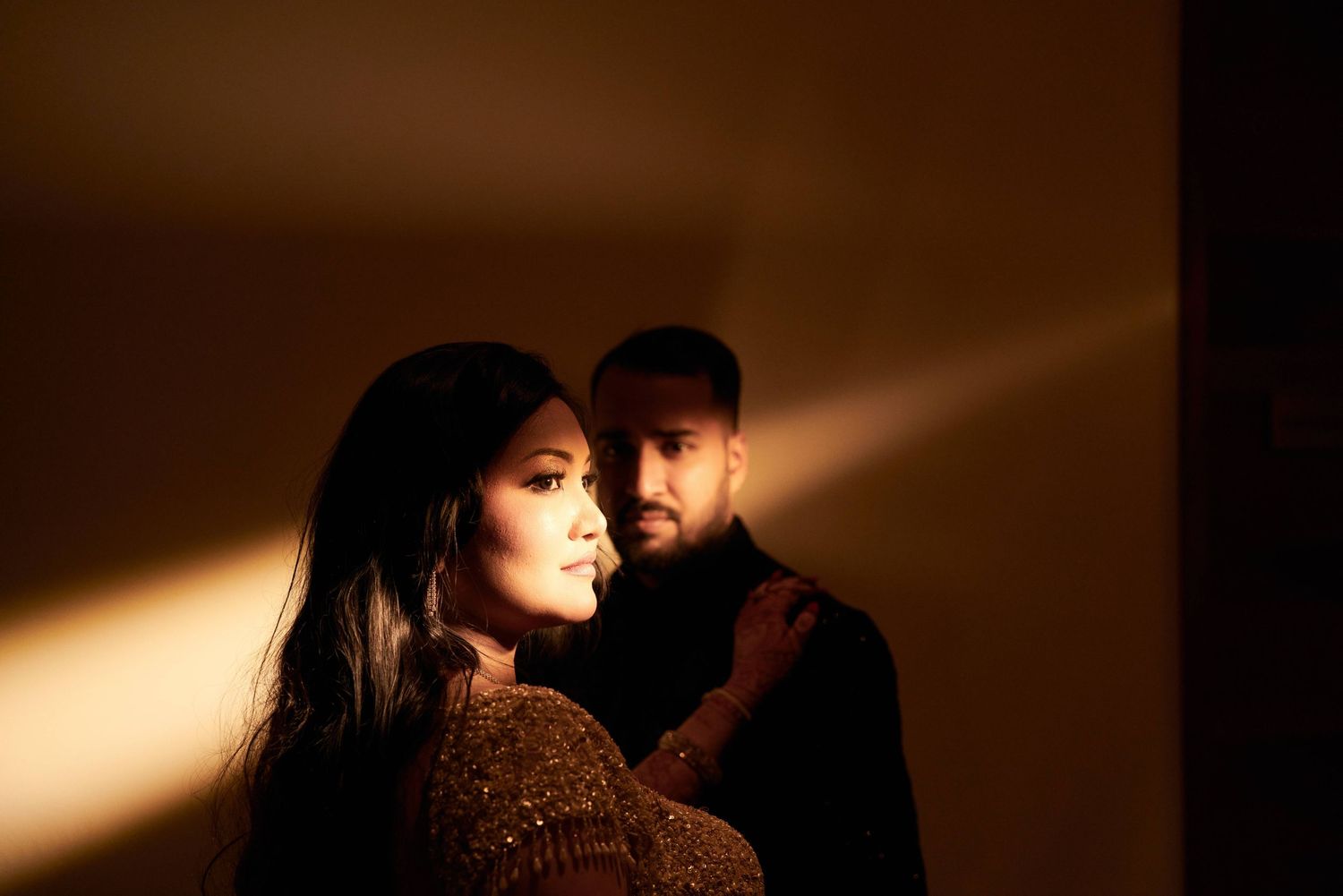 Couple in warm golden light with dramatic shadows in intimate portrait setting.
