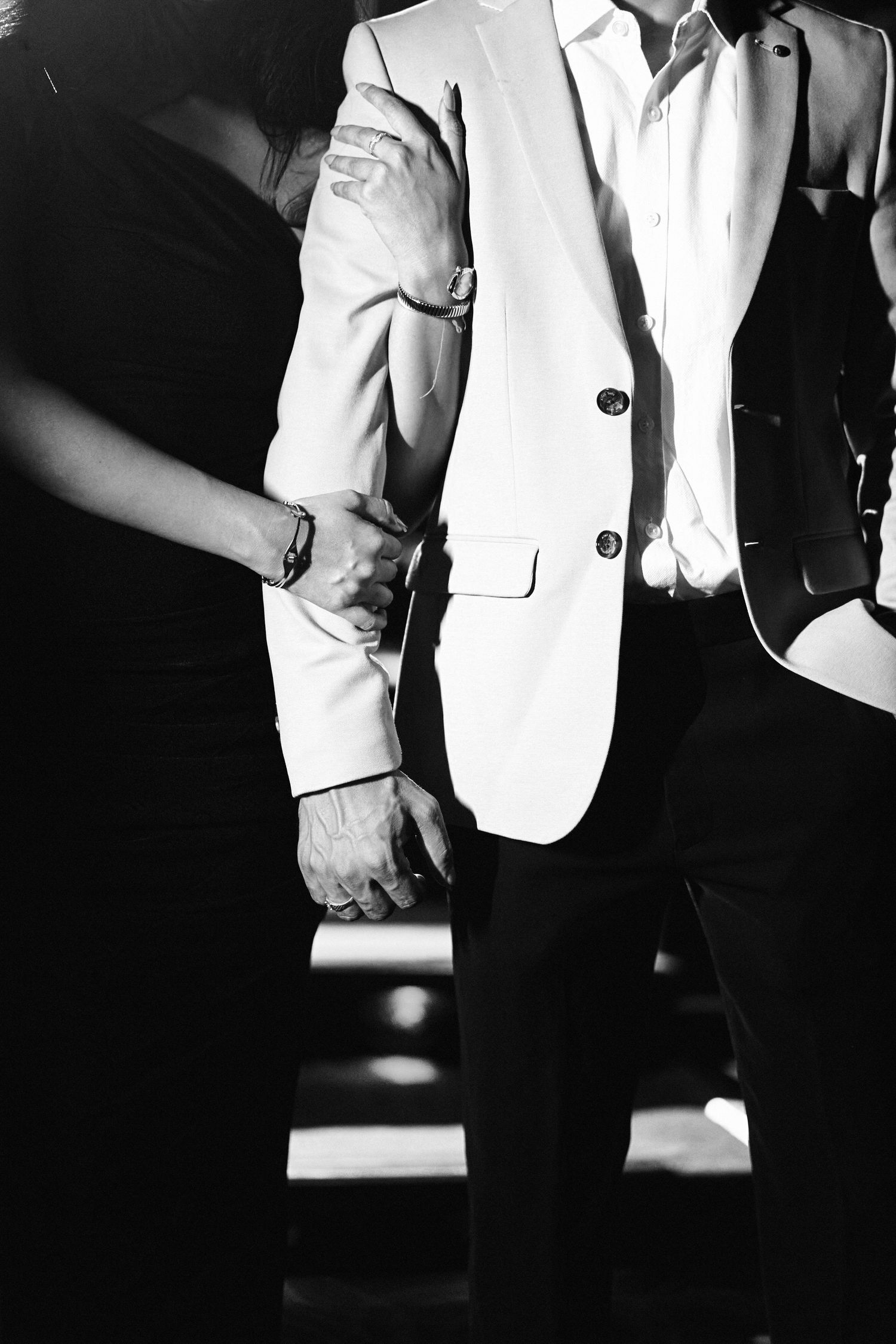 Black and white photo of an elegant couple holding hands, man in white blazer and woman in black dress.