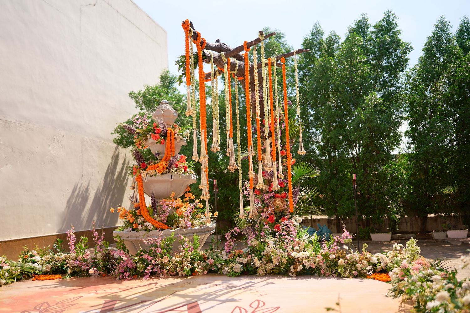 Outdoor Indian wedding ceremony decor with orange marigold garlands, wooden arch, and lush floral arrangements.