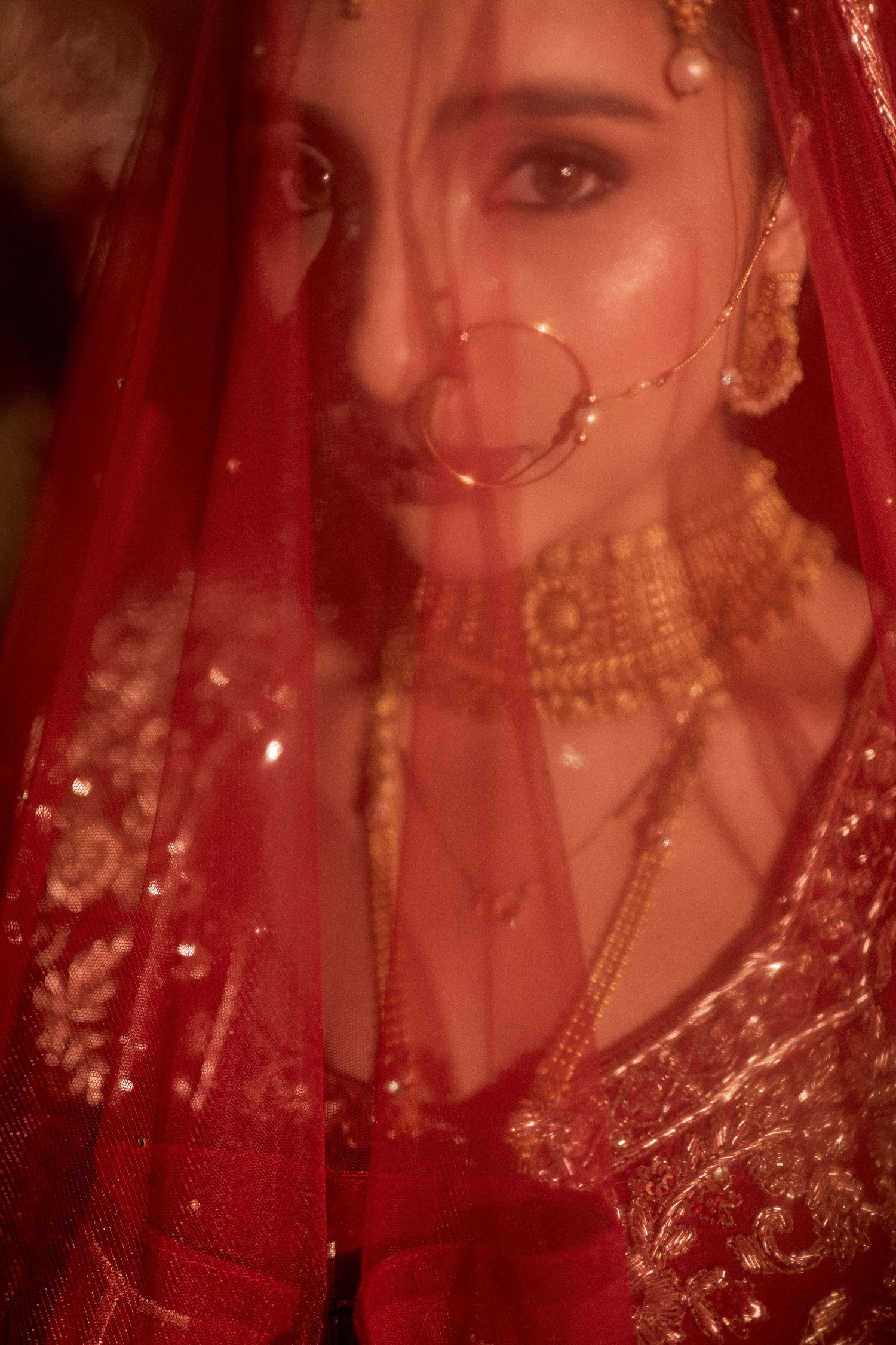 Indian bride in red lehenga and veil with gold choker necklace and nose ring for traditional wedding.