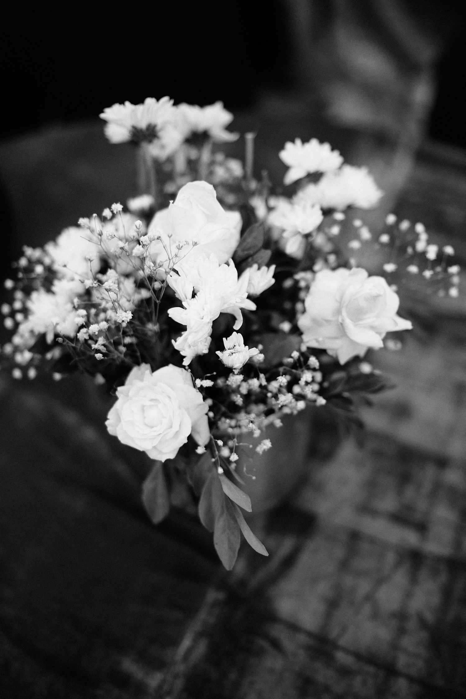 A black and white close-up of a delicate floral arrangement featuring white roses and baby's breath on a table.
