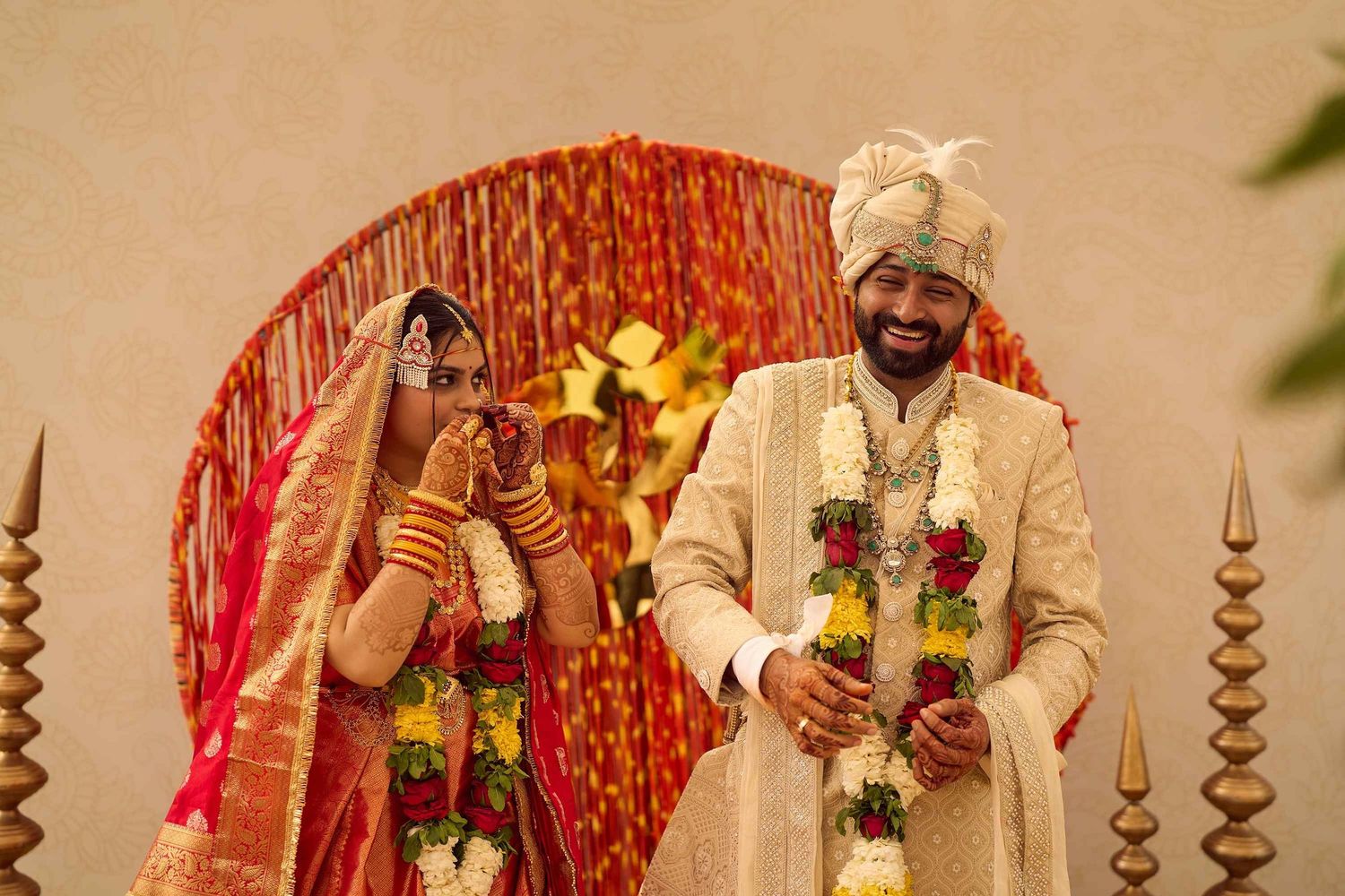 Indian bride and groom laughing joyfully during traditional Hindu wedding ceremony with floral garlands.
