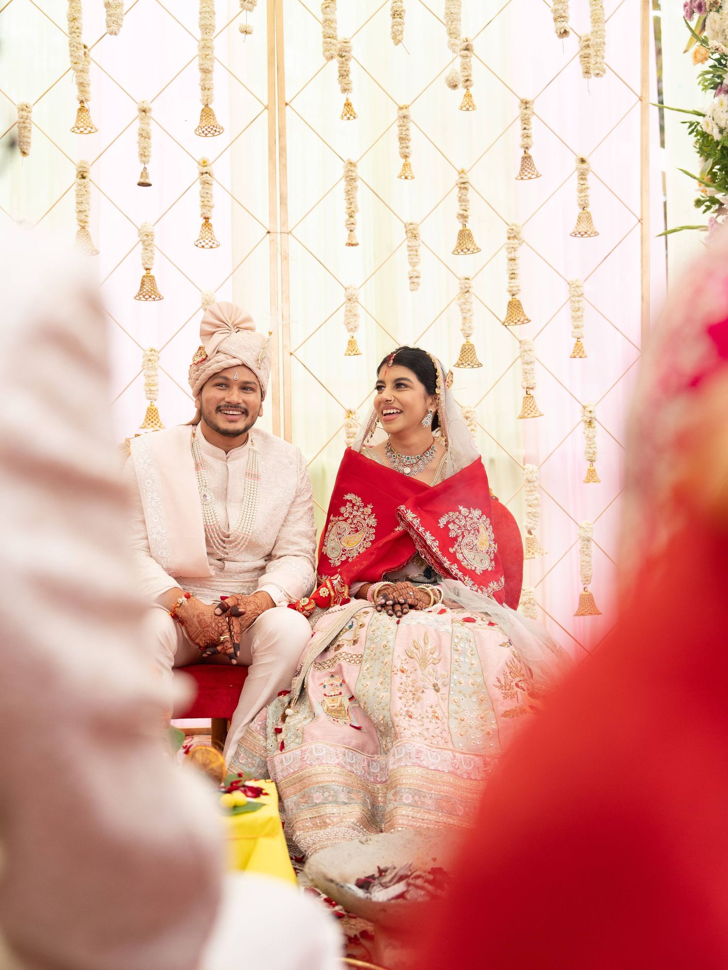Indian couple in traditional wedding attire seated during ceremony with gold decorative backdrop.