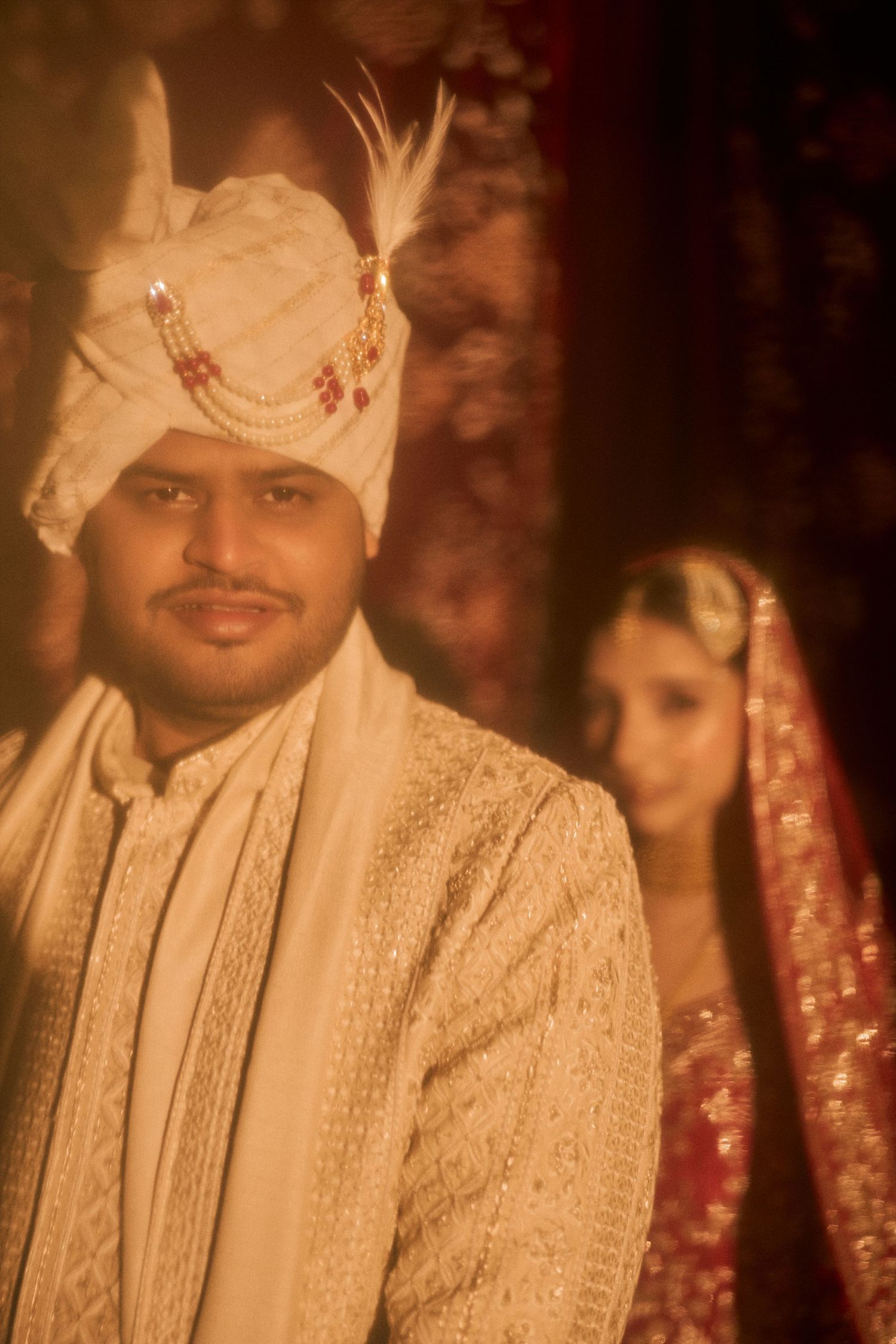 Groom in white sherwani and turban with bride in red lehenga at a traditional Indian wedding ceremony.