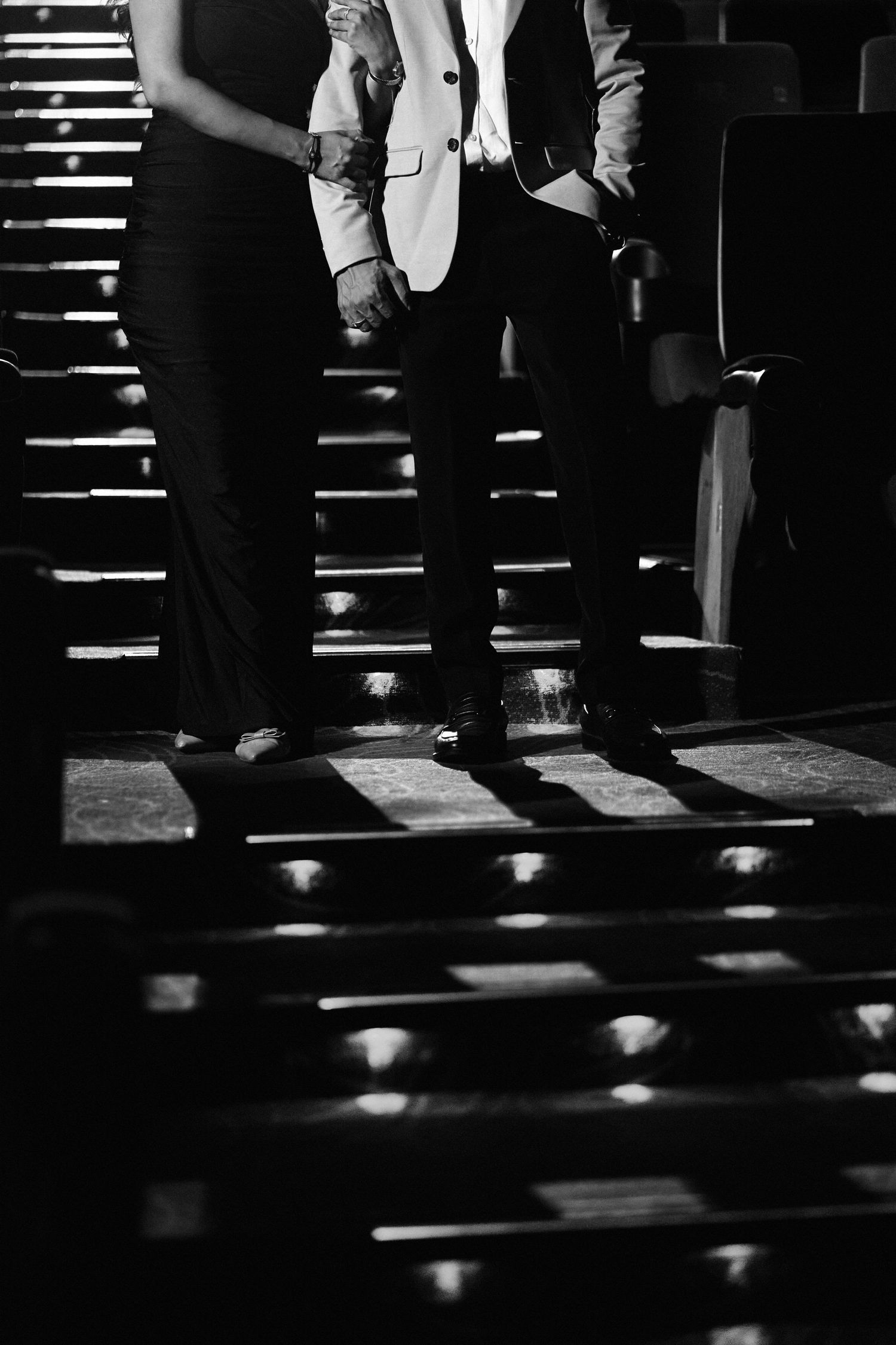 Black and white photo of two people standing on stairs, one wearing a white blazer and dark trousers.