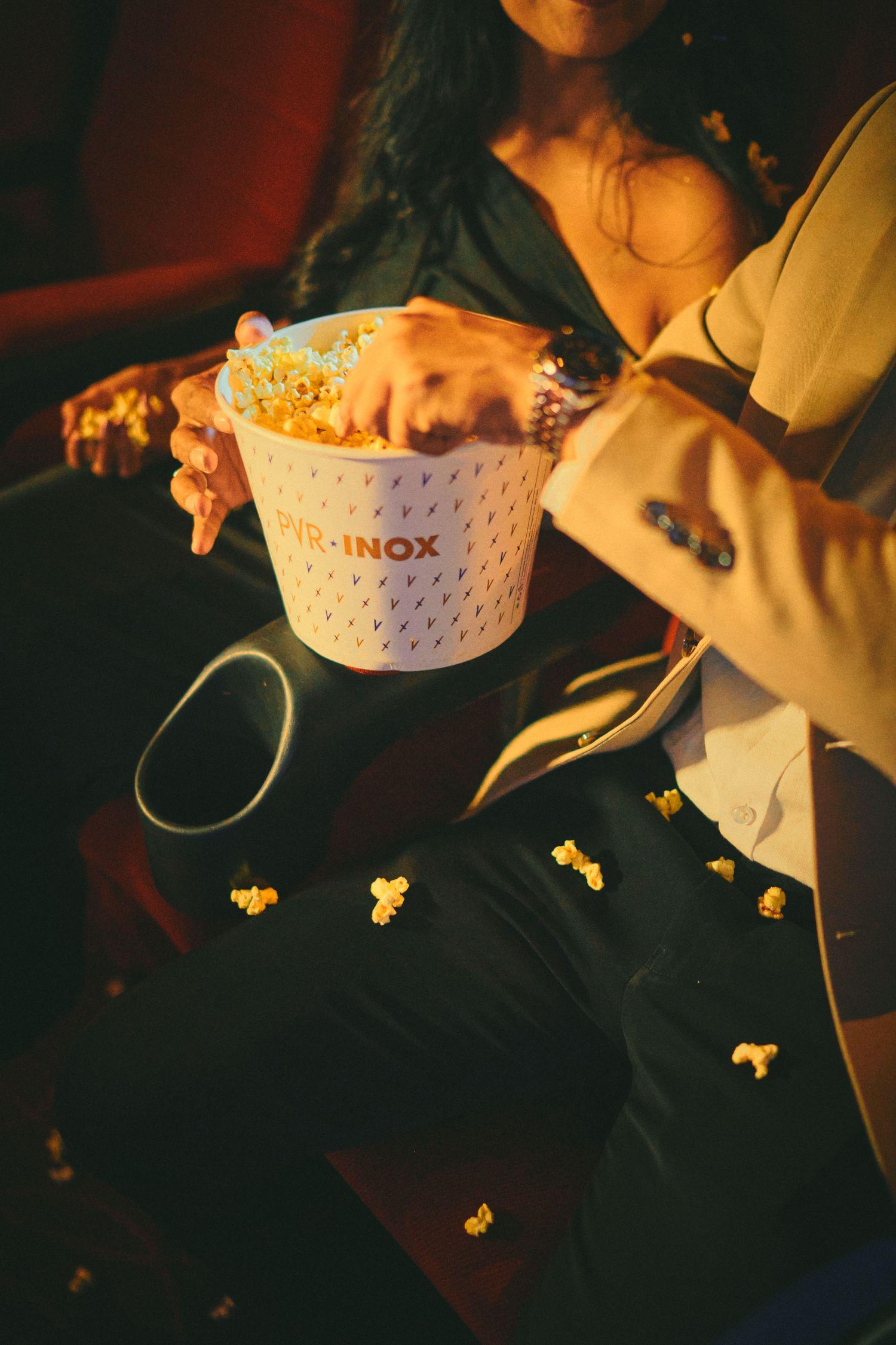 Two people sharing a bucket of popcorn at a cinema, with scattered popcorn on their laps.
