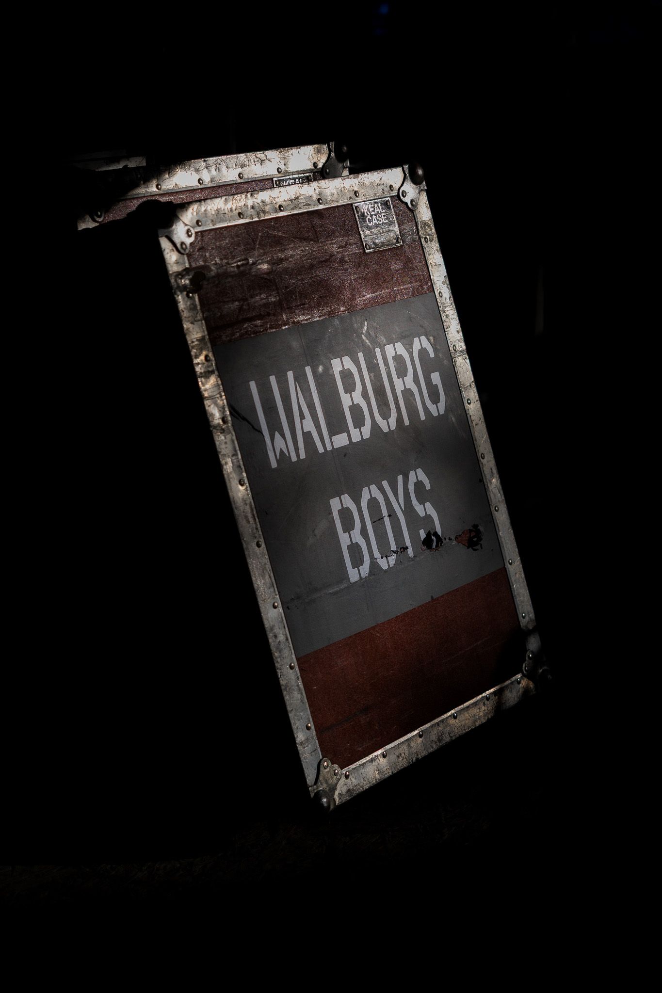 Vintage weathered case reading Walburg Boys illuminated against a dark black background.