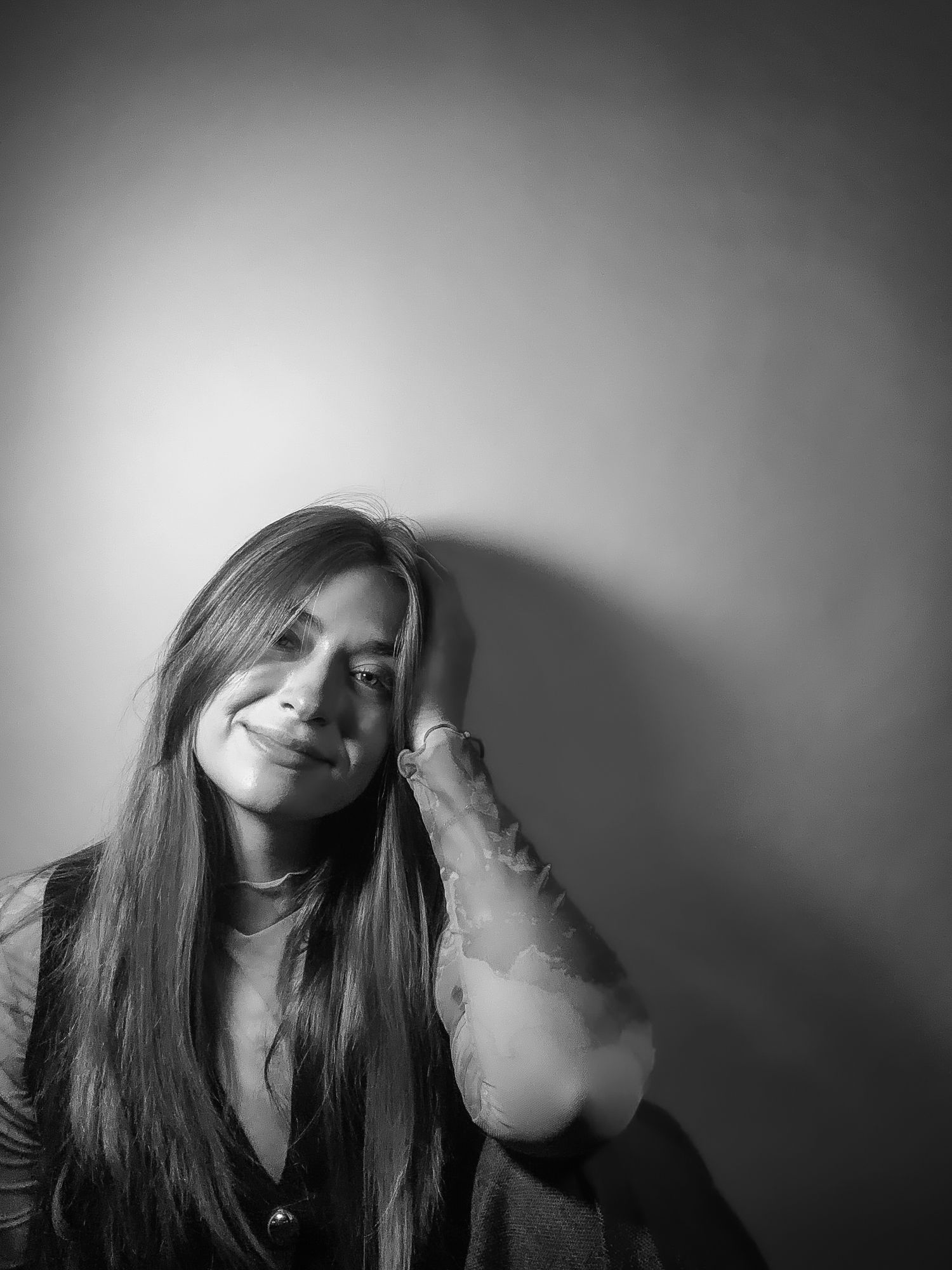 Black and white portrait of smiling young woman resting head on hand against wall.
