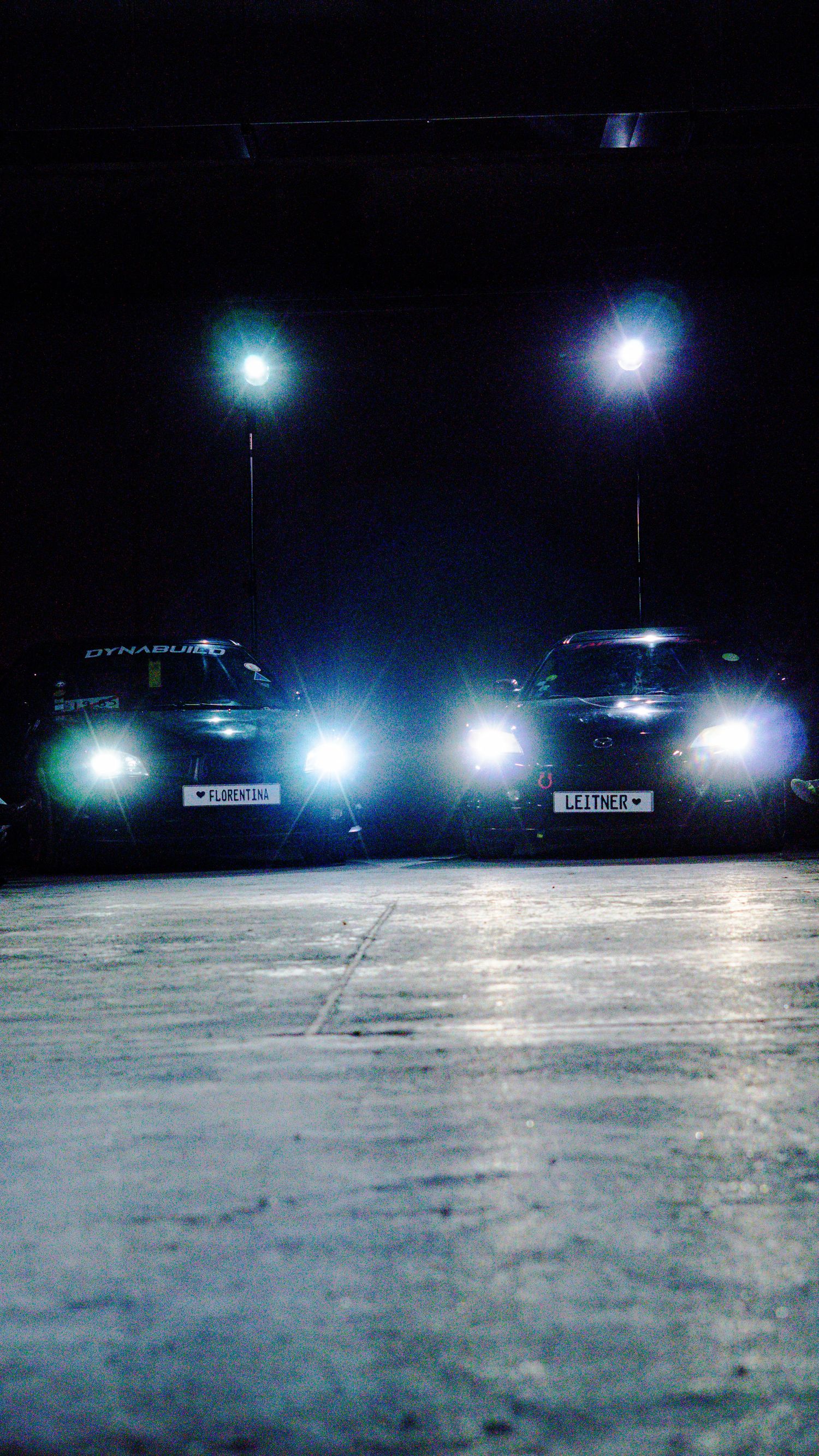 Two cars with bright headlights parked in a dark garage serving as a fashion show runway backdrop.