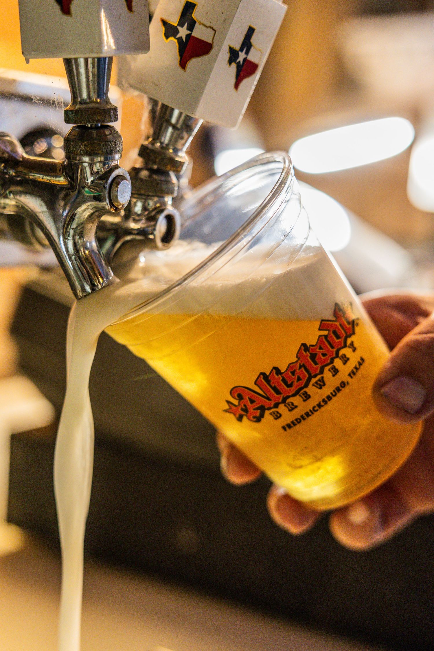 Hand holding an Altstadt Brewery glass being filled with golden beer from a tap at a biergraten in Walburg, Texas.