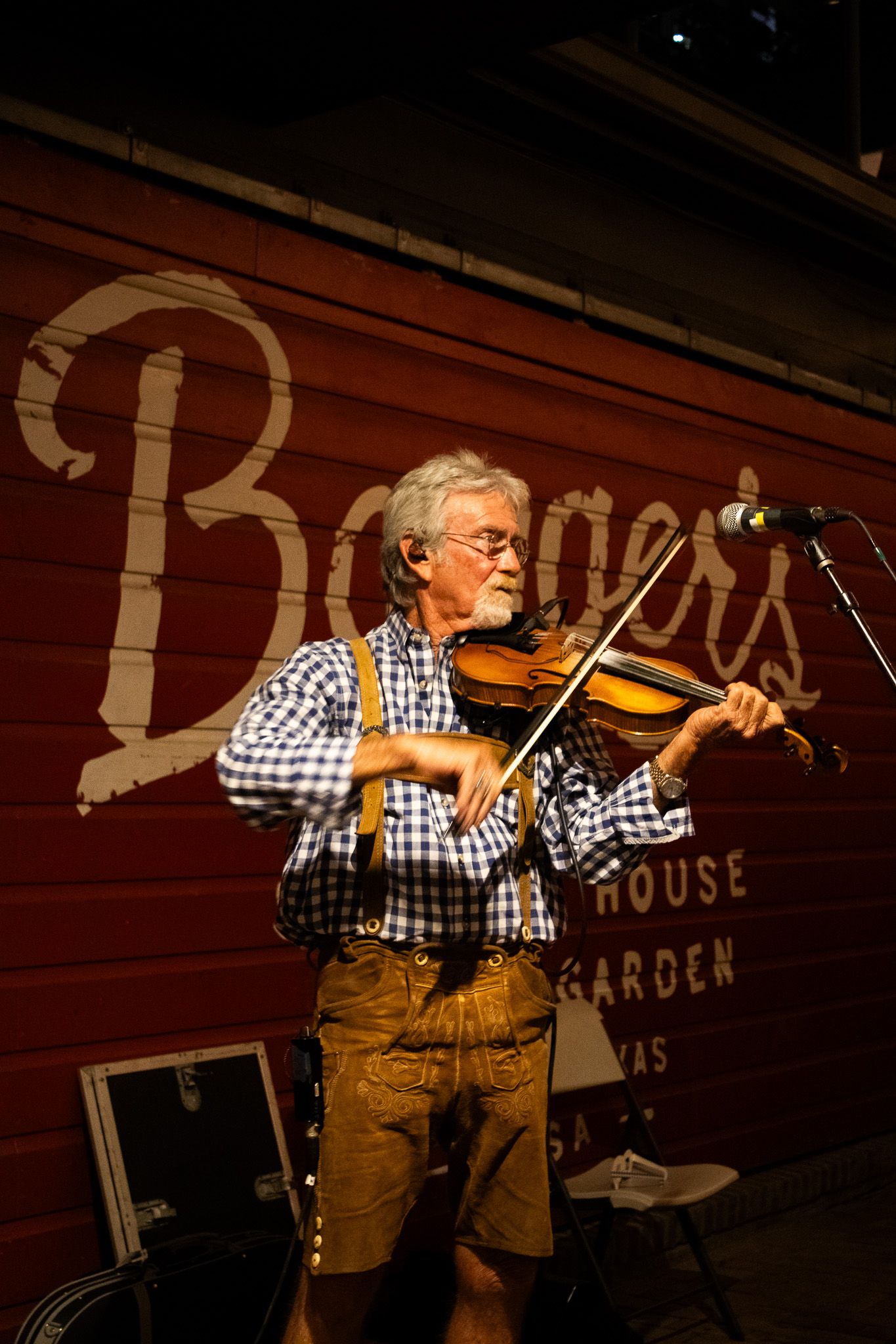 Older man plays fiddle on stage in front of a Bangers beer garden sign in Austin, Texas.