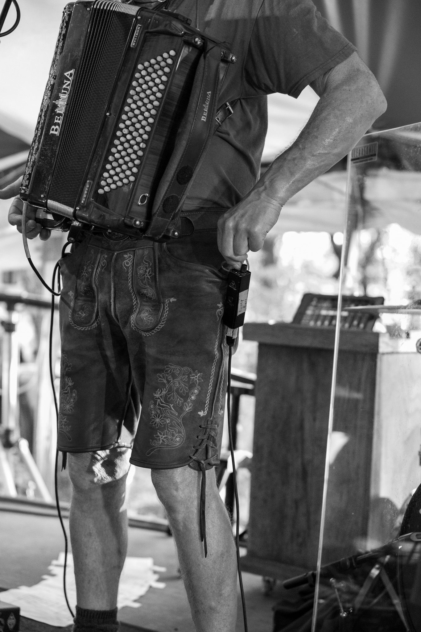 Black and white photo of a musician playing a Bernina accordion while wearing leather lederhosen.