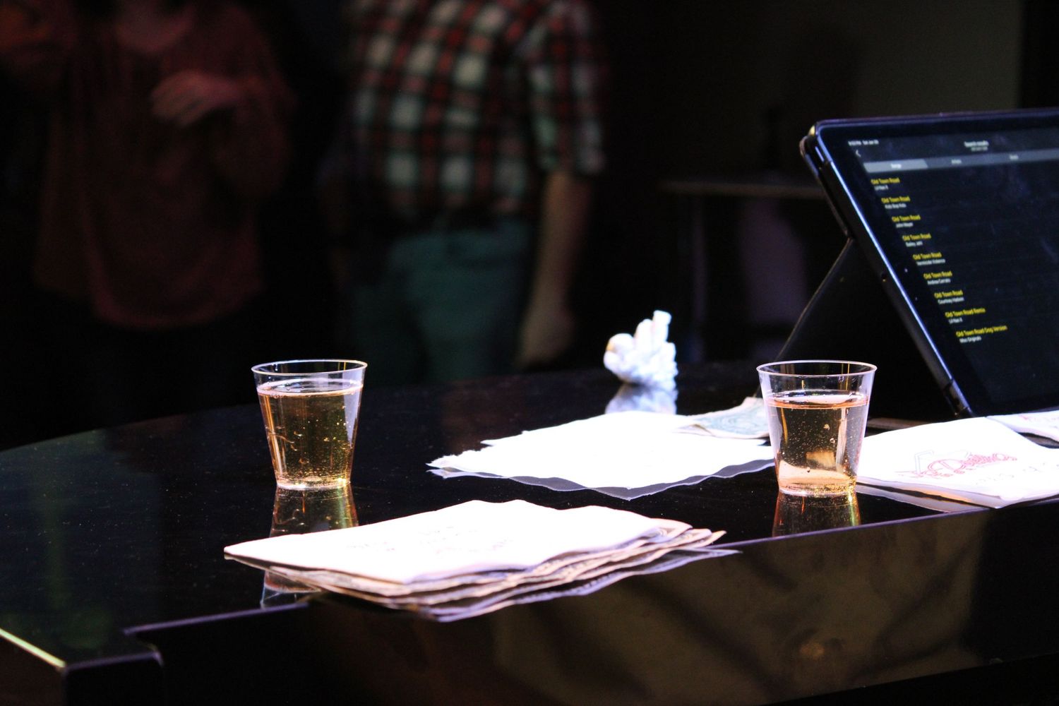 Two plastic cups of beer on a piano beside napkins at a live event.