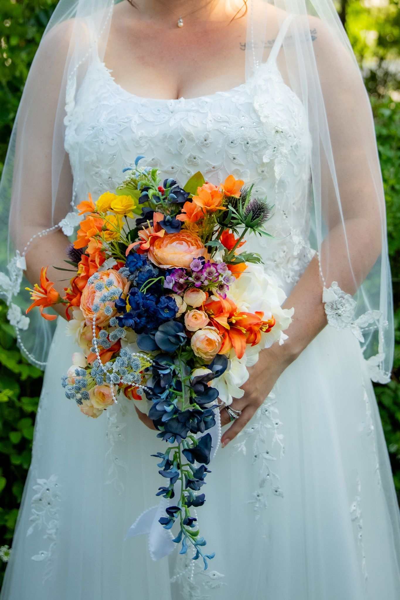 Bride in white lace gown holding a vibrant cascading bouquet of colorful flowers.