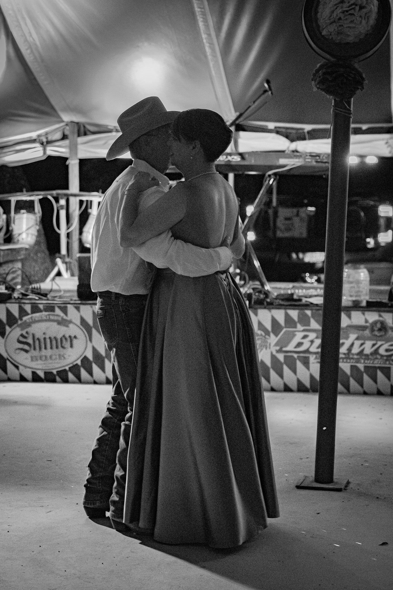 Black and white photo of a couple in western attire sharing a kiss at an outdoor event.