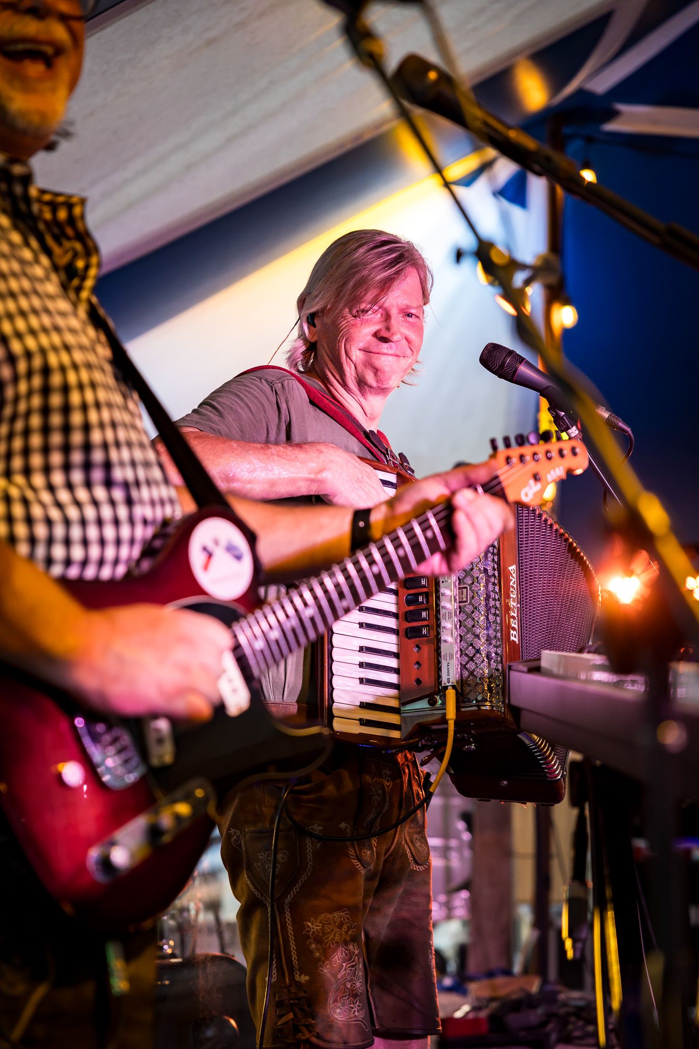 Musician playing red electric guitar and accordion on stage at a live performance.