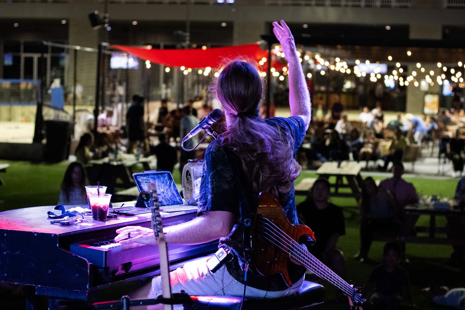Male bassist performs on outdoor stage at night, raising hi hand to the crowd.