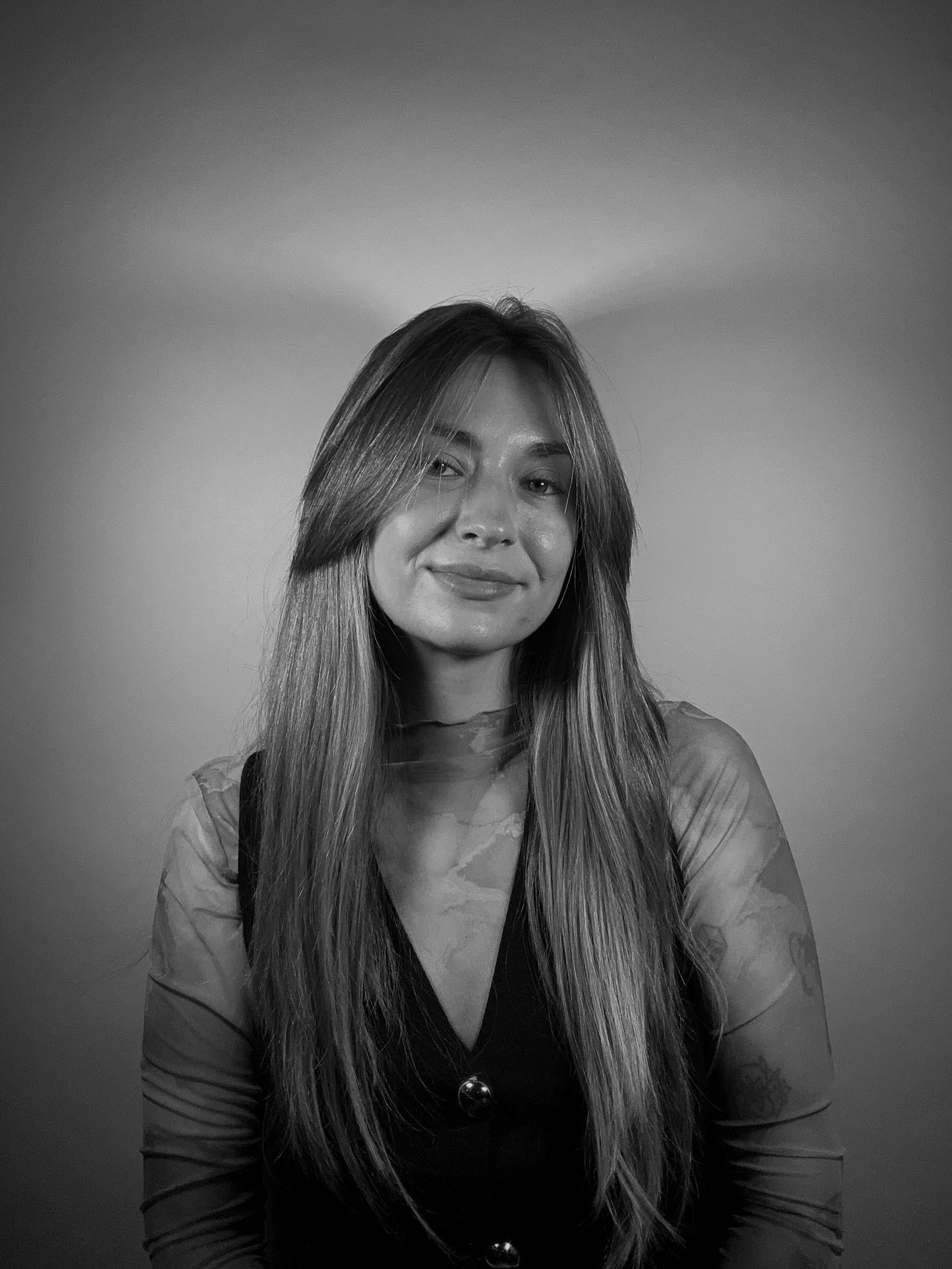 Black and white studio portrait of smiling young woman with long straight hair.