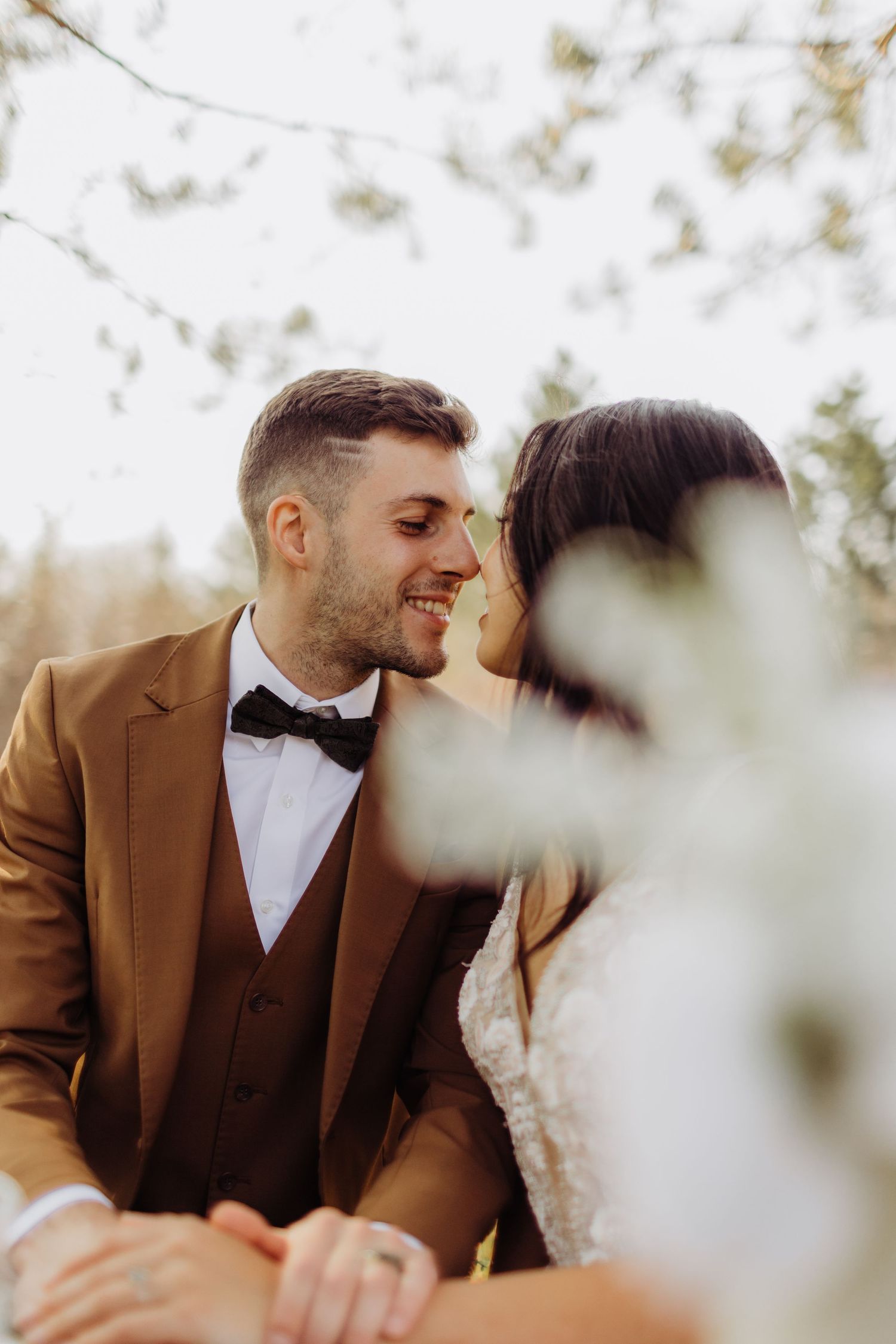 A bride and groom sharing an intimate moment at their table toughing noses, with florals slightly blocking them