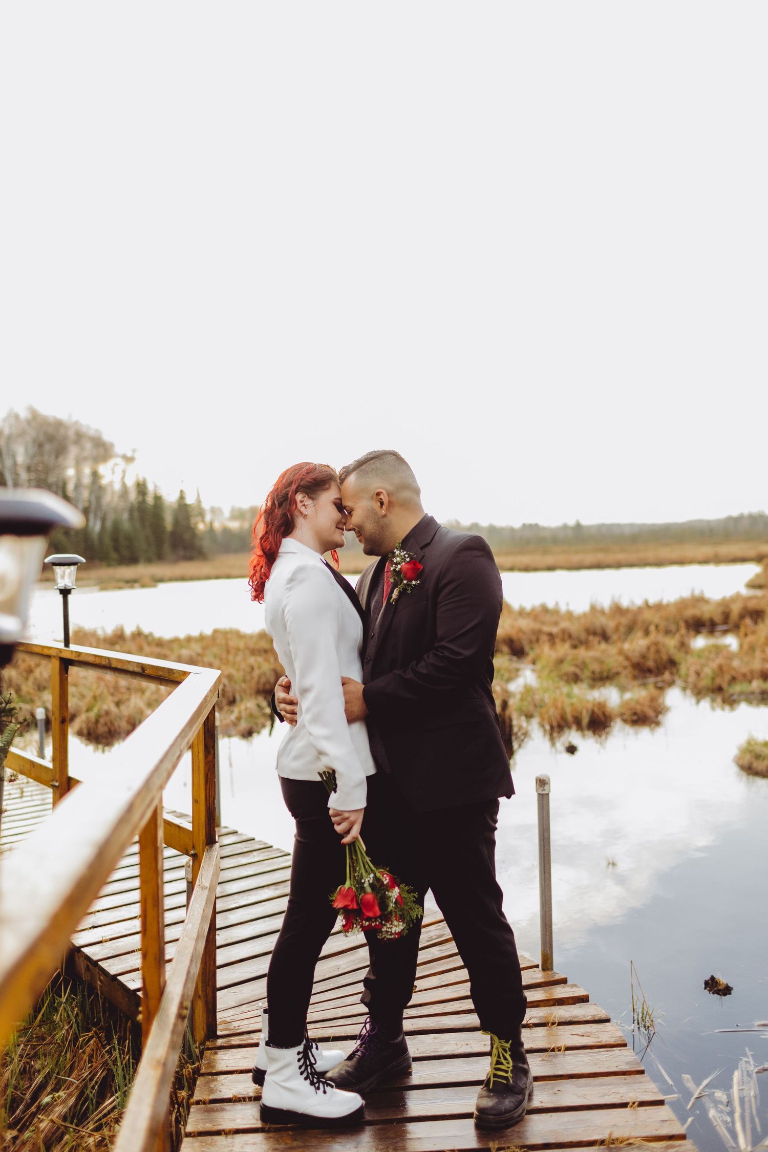 bride and groom couple standing on a floating dock over a watershed area, touching foreheads.