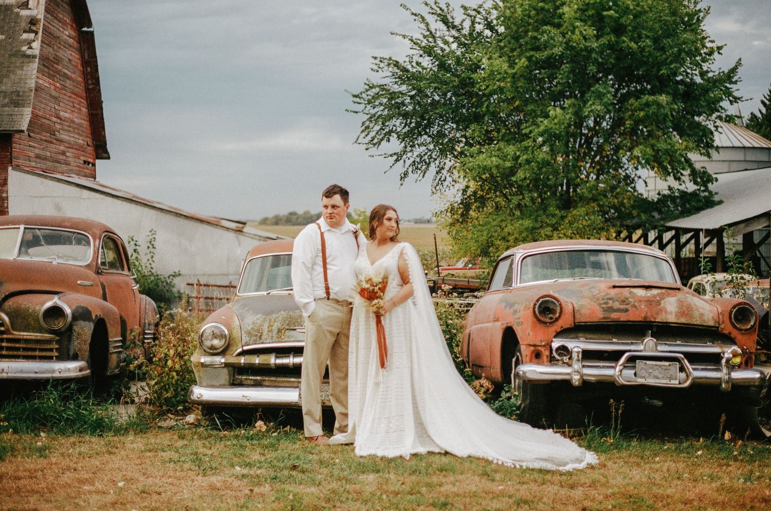 Bride and groom looking opposite directions in front of three old cars.