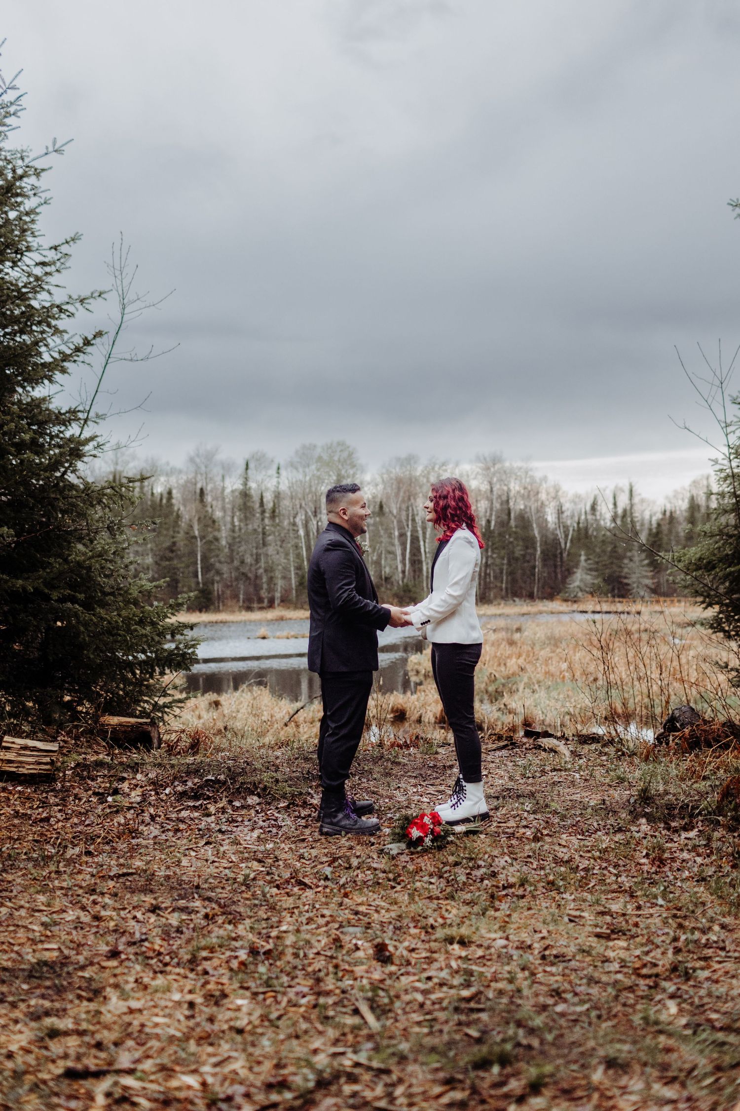 Bride and Groom holding hands and exchanging vows on a hill in front of a watershed area. With flowers on the ground.