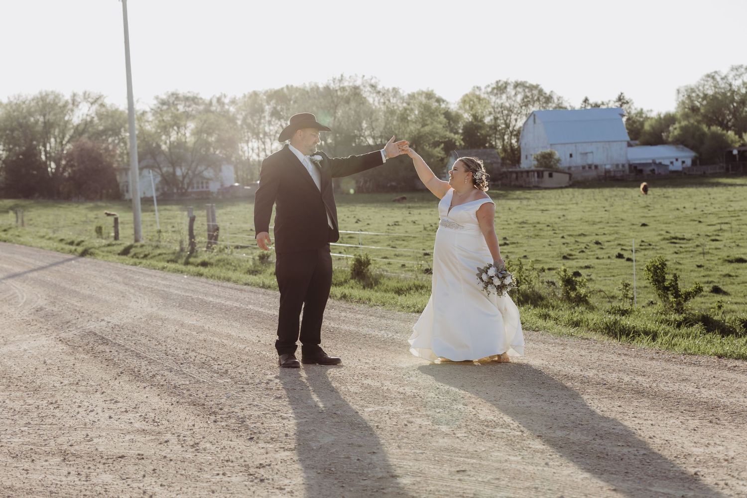 Bride and Groom dancing on a gravel road in front of a highland cow farm.