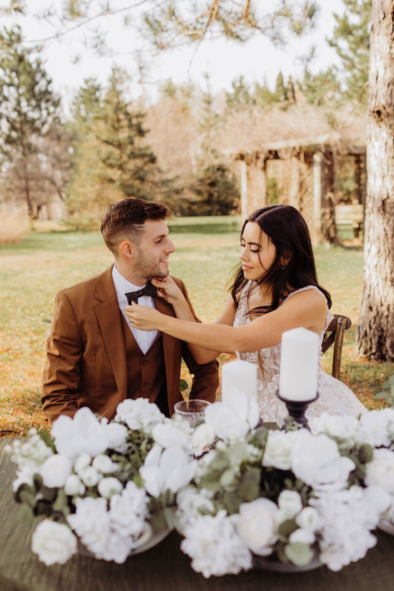 bride and groom sitting at their table, the bride is straightening the grooms bow tie.