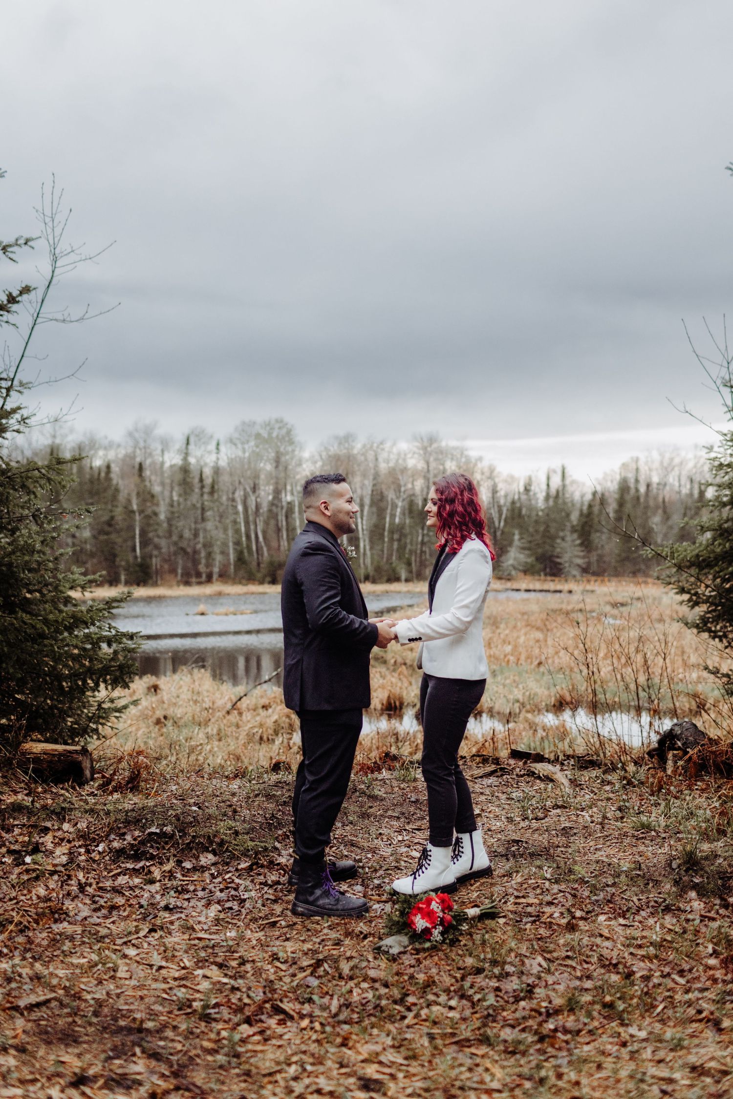 Bride and Groom holding hands and exchanging vows on a hill in front of a watershed area. With flowers on the ground.