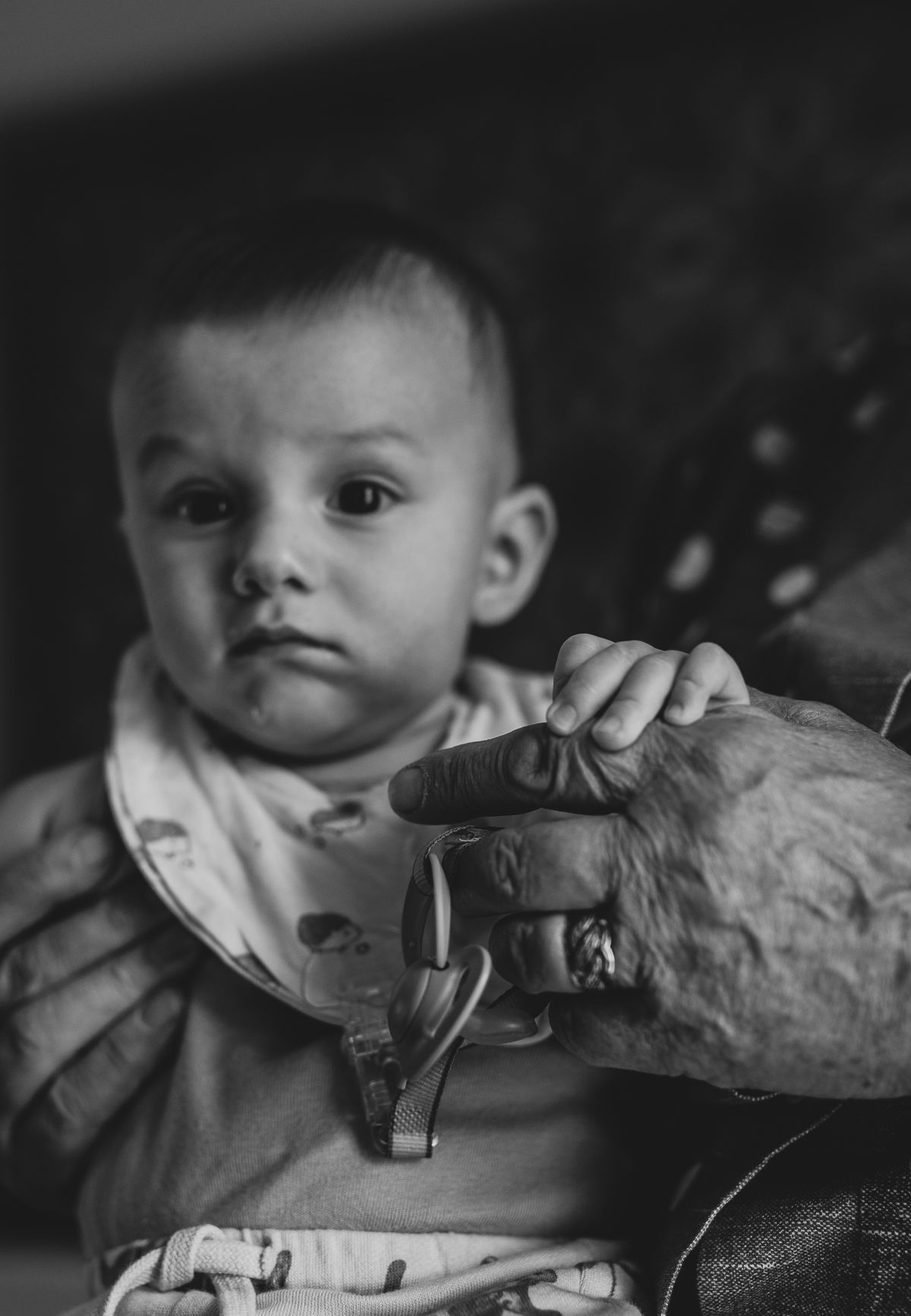 Black and white photo of a baby holding grandmother's hands during a family photoshoot indoors