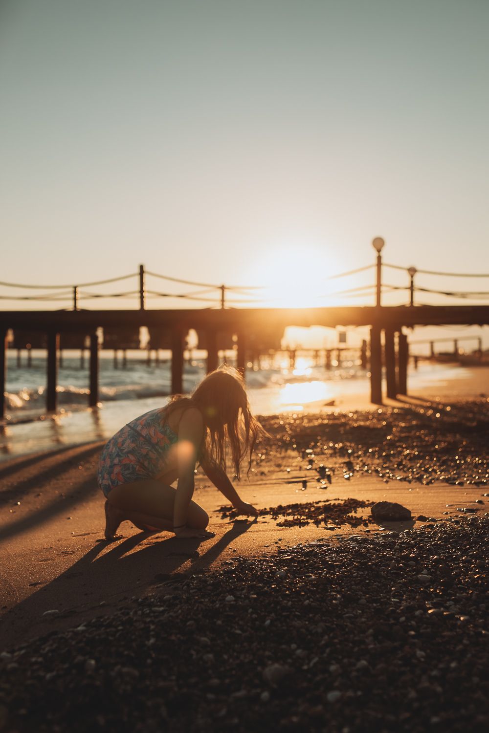 Child playing on the beach at sunset, drawing in the sand, lifestyle family photography outdoors.