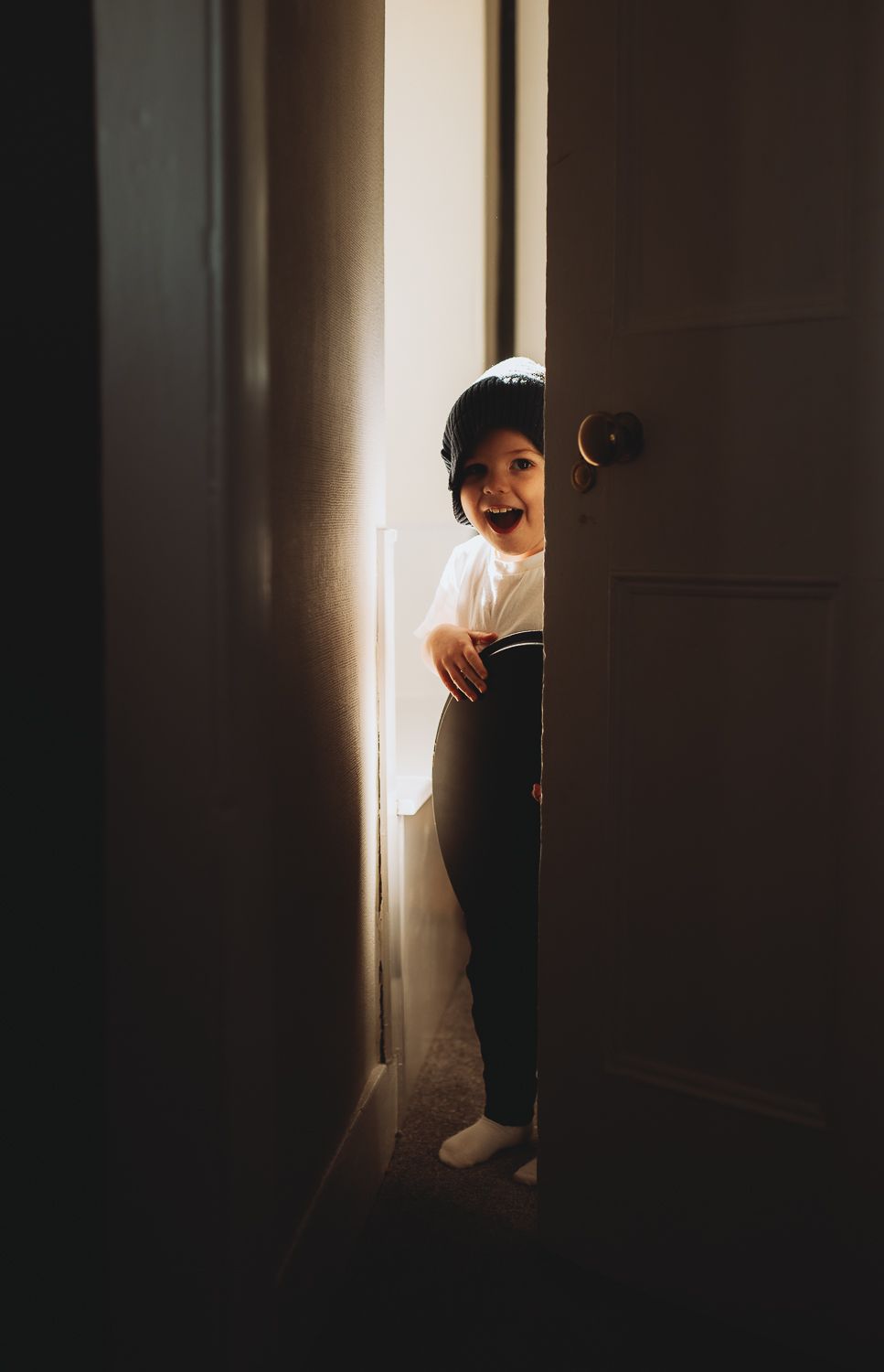A toddler captured peeking out of the room, documentary-style family photography capturing everyday life