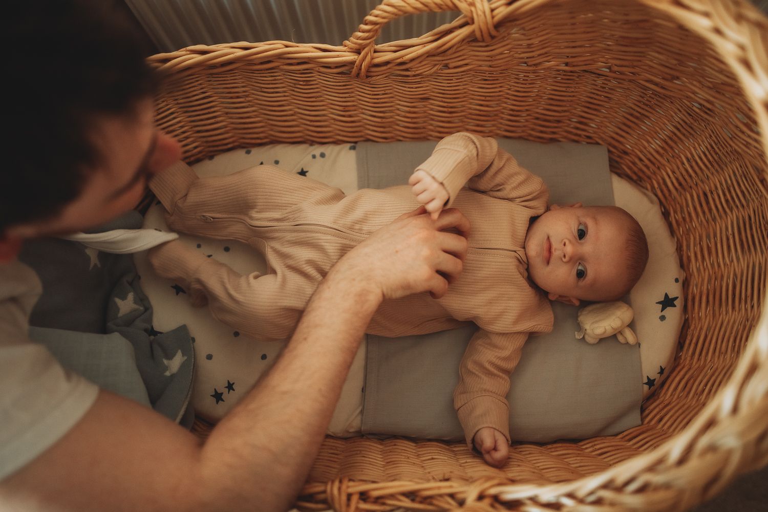 Baby in basinet, father stretching out to play with the baby, documentary-style family photography capturing everyday life